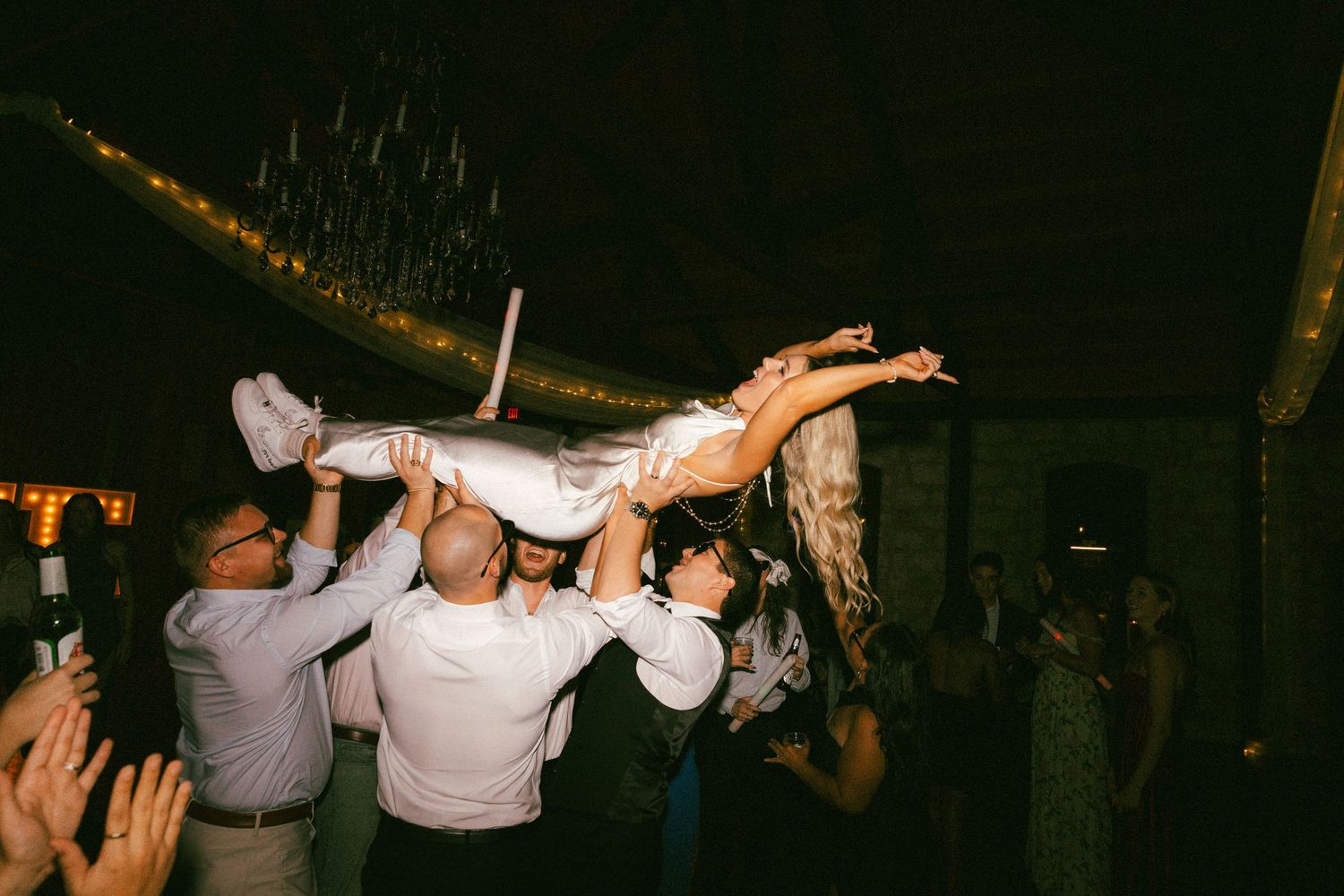 Guests lift the bride above the crowd during a lively wedding reception dance floor celebration.