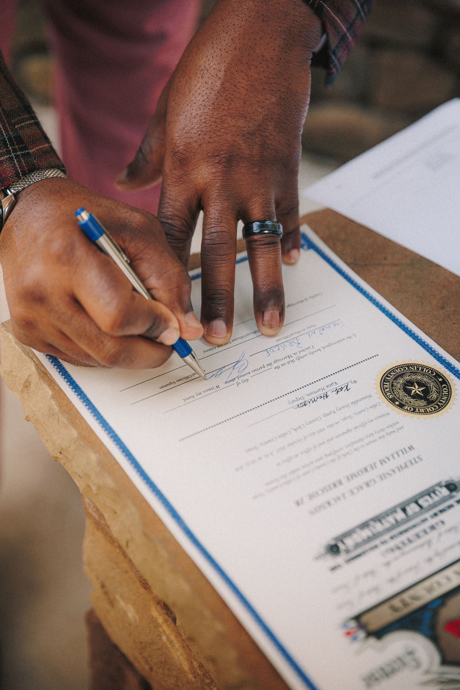 Groom signing official wedding marriage certificate with blue pen wearing wedding band.