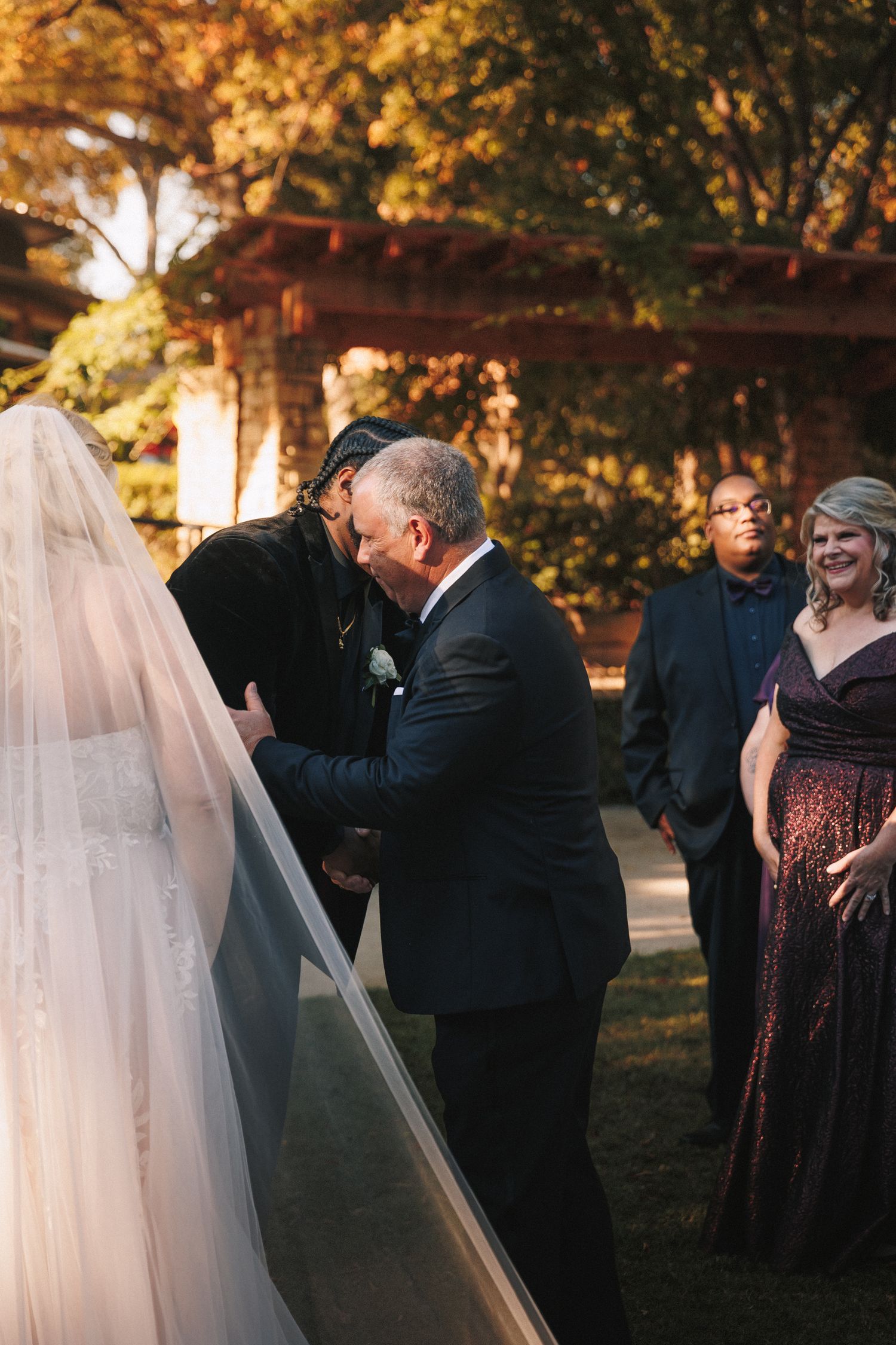 Father of the bride sharing an emotional first look moment with his daughter in a white wedding gown and veil outdoors.
