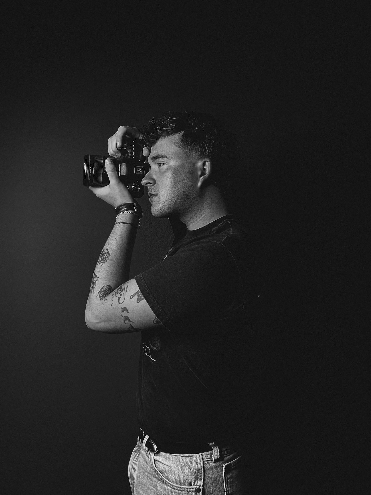 Moody black and white portrait of someone holding a camera in side profile against a dark background.