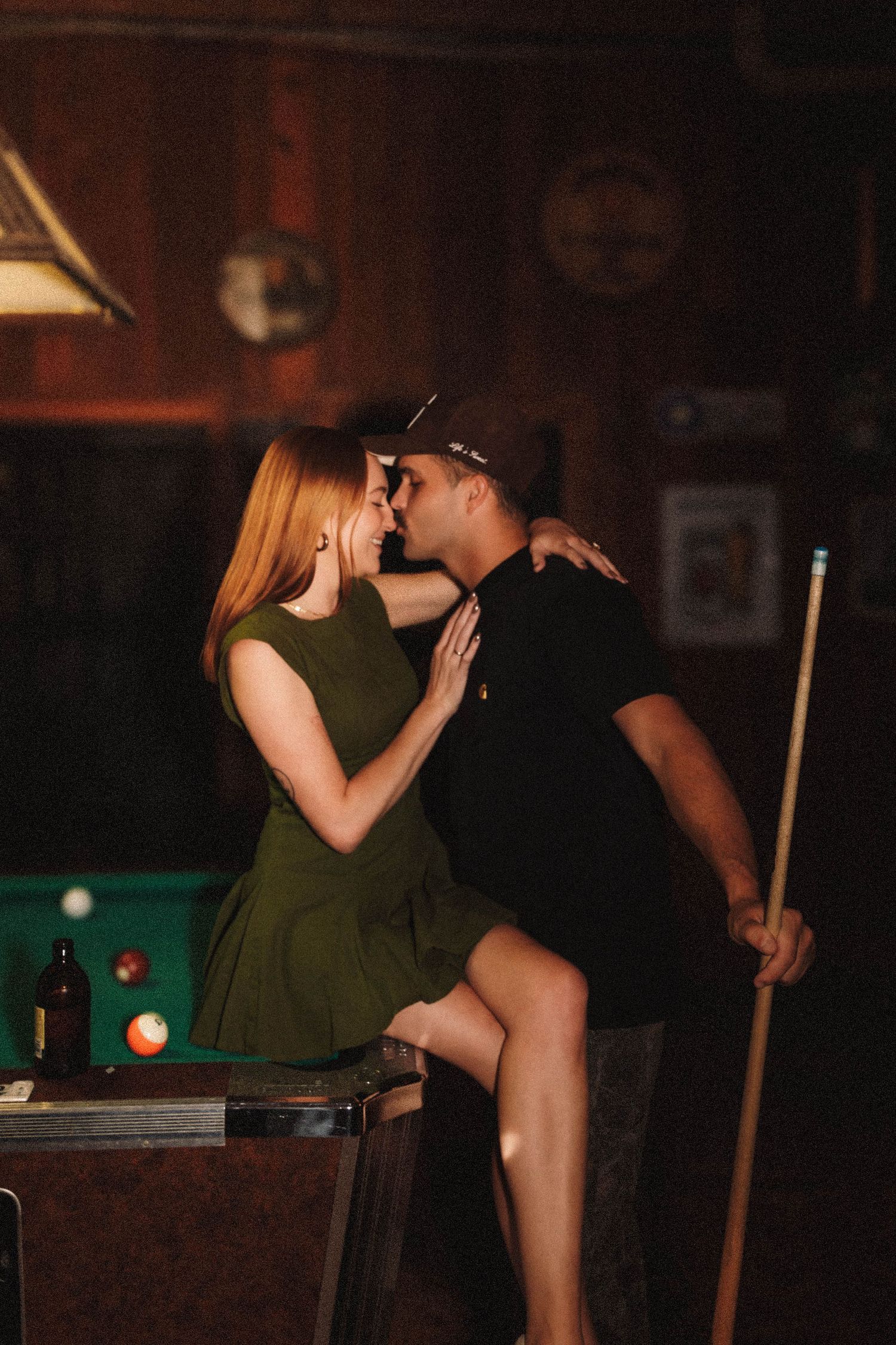 Two people playing billiards at a bar in dark, moody lighting conditions.