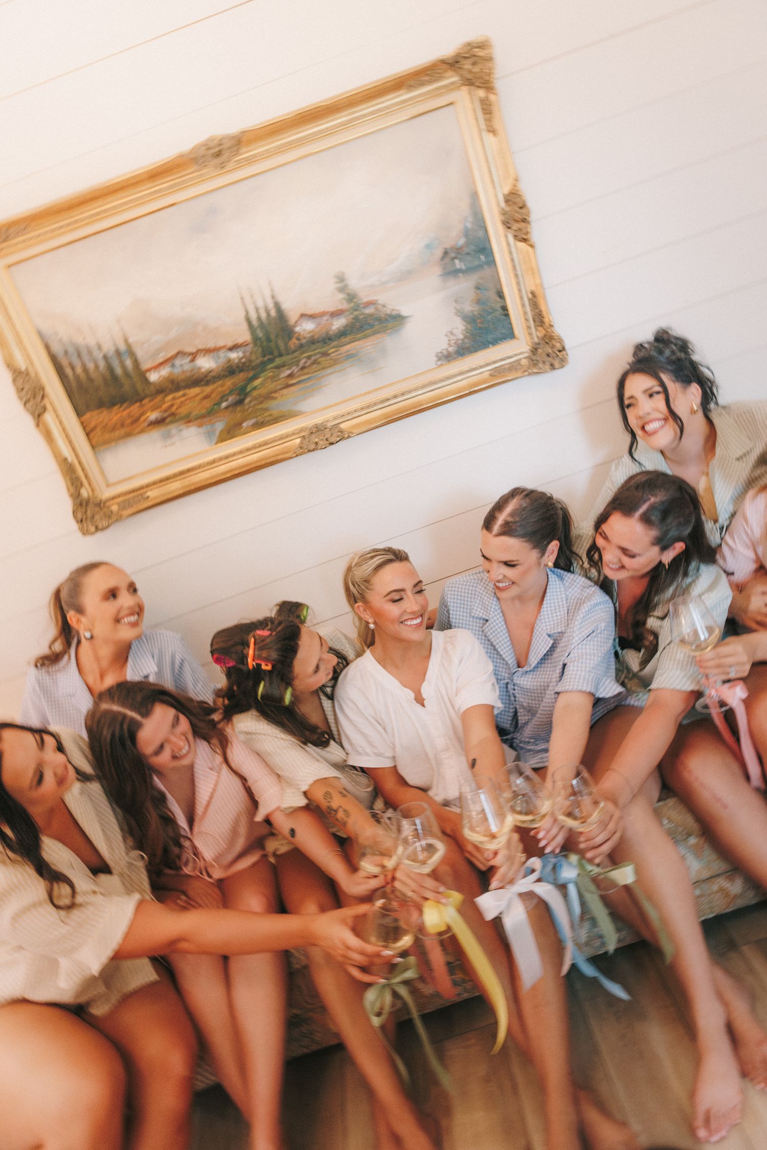 Celebration scene with friends toasting champagne glasses while sitting together indoors near a framed landscape painting.