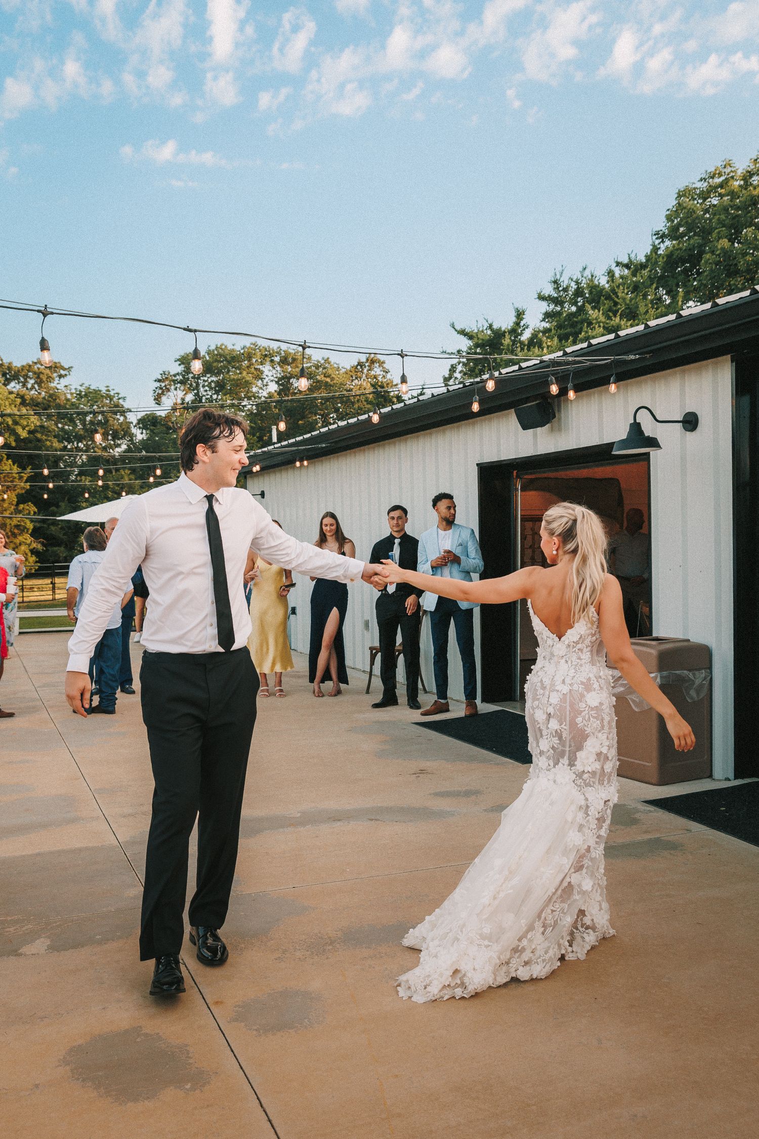 Wedding couple dancing together on an outdoor patio under string lights at sunset.