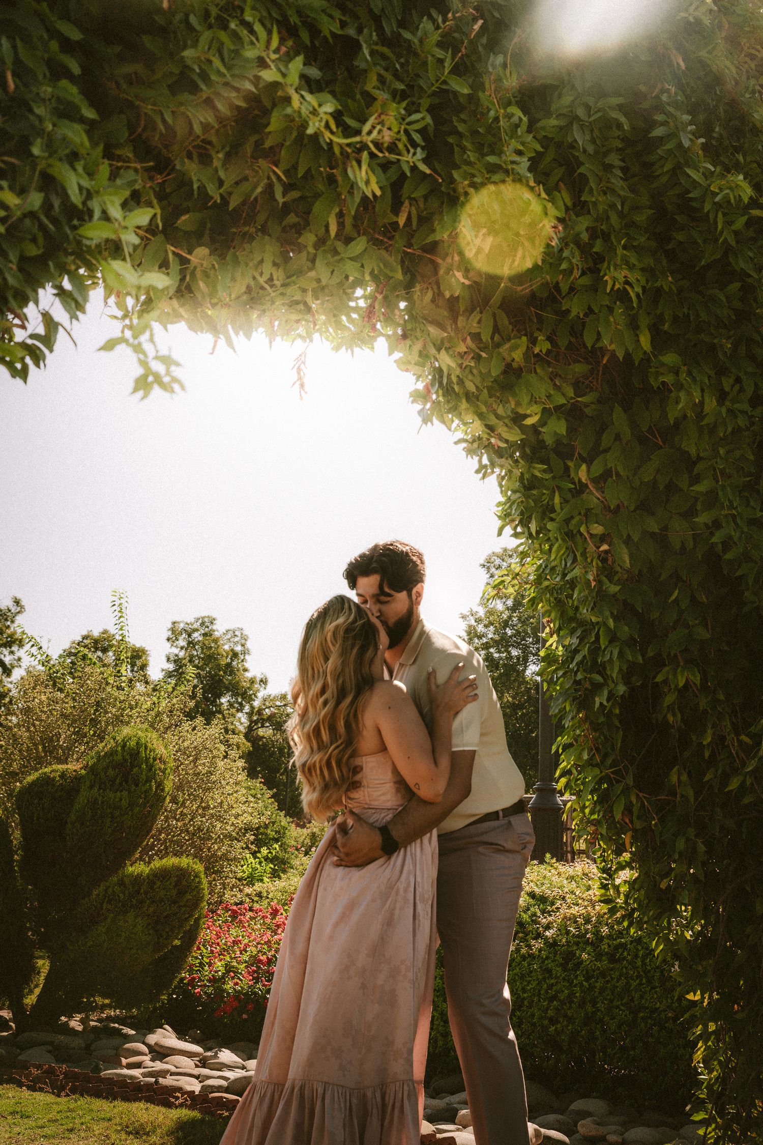 A tender embrace captured under lush green foliage in a garden setting.