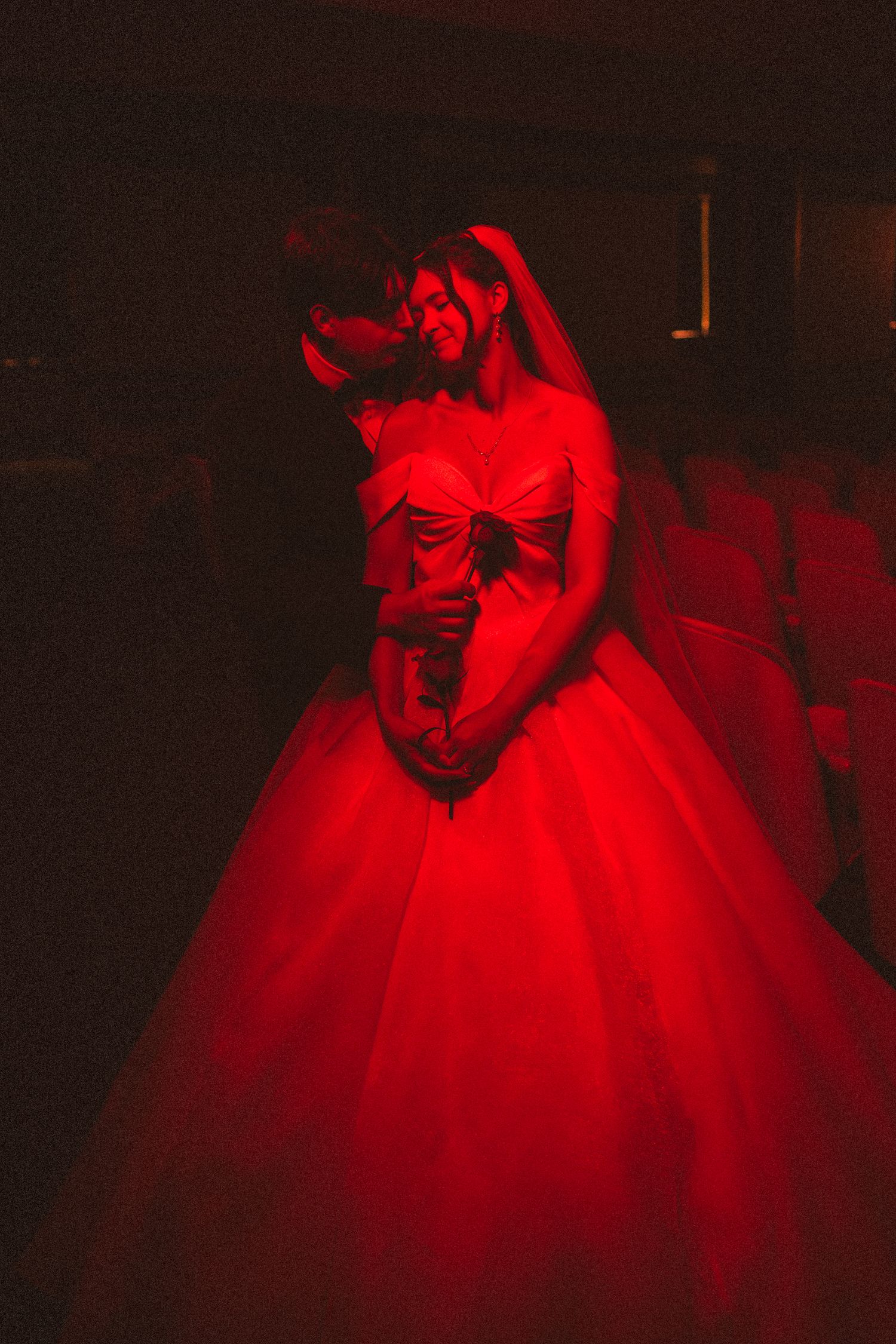 Bride and groom embracing in dramatic red light wearing stunning ballgown wedding dress.