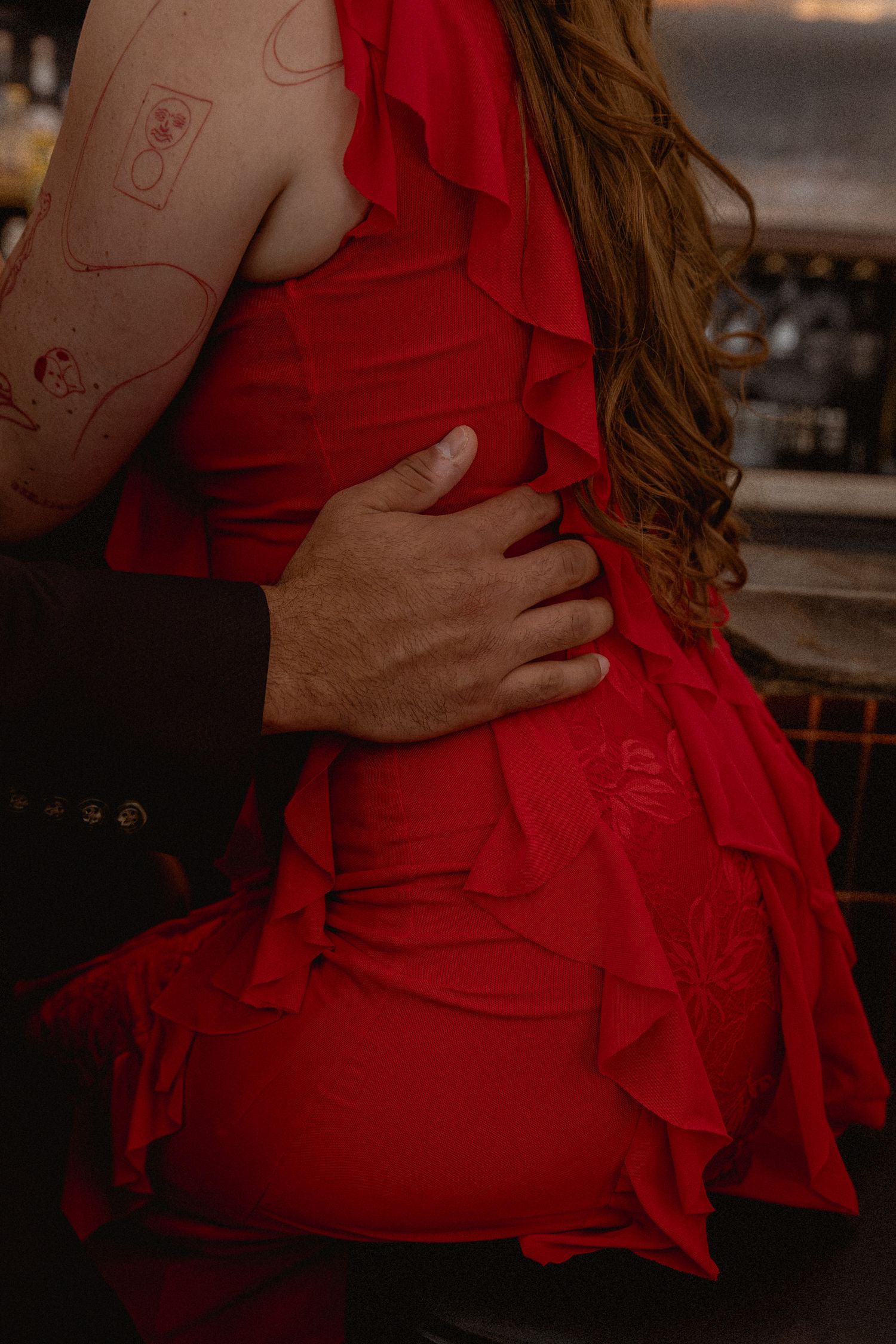 Woman in red ruffled dress embraced from behind by a man's hand around her waist.