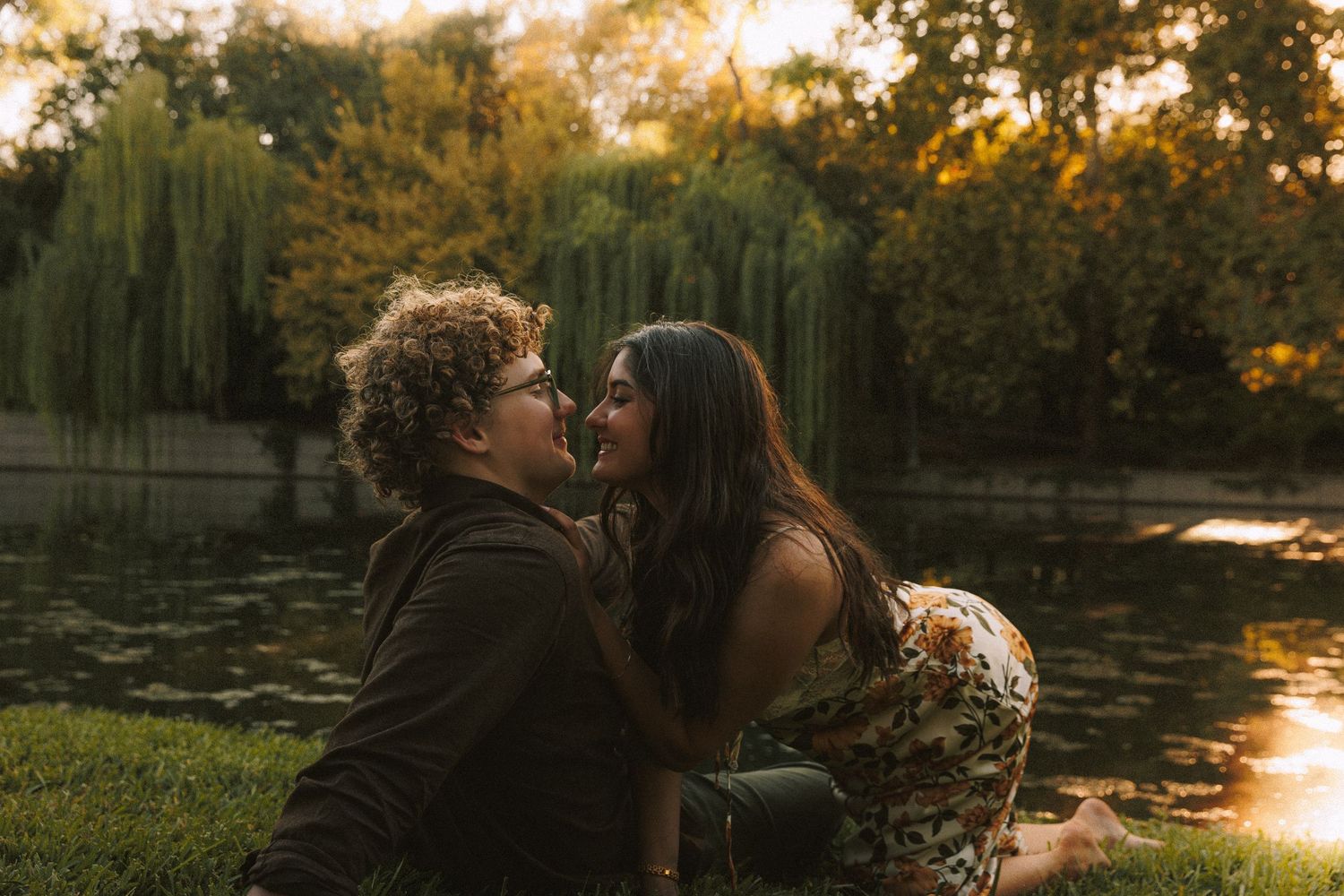Romantic sunset scene by a willow tree-lined pond with golden light reflecting on water.