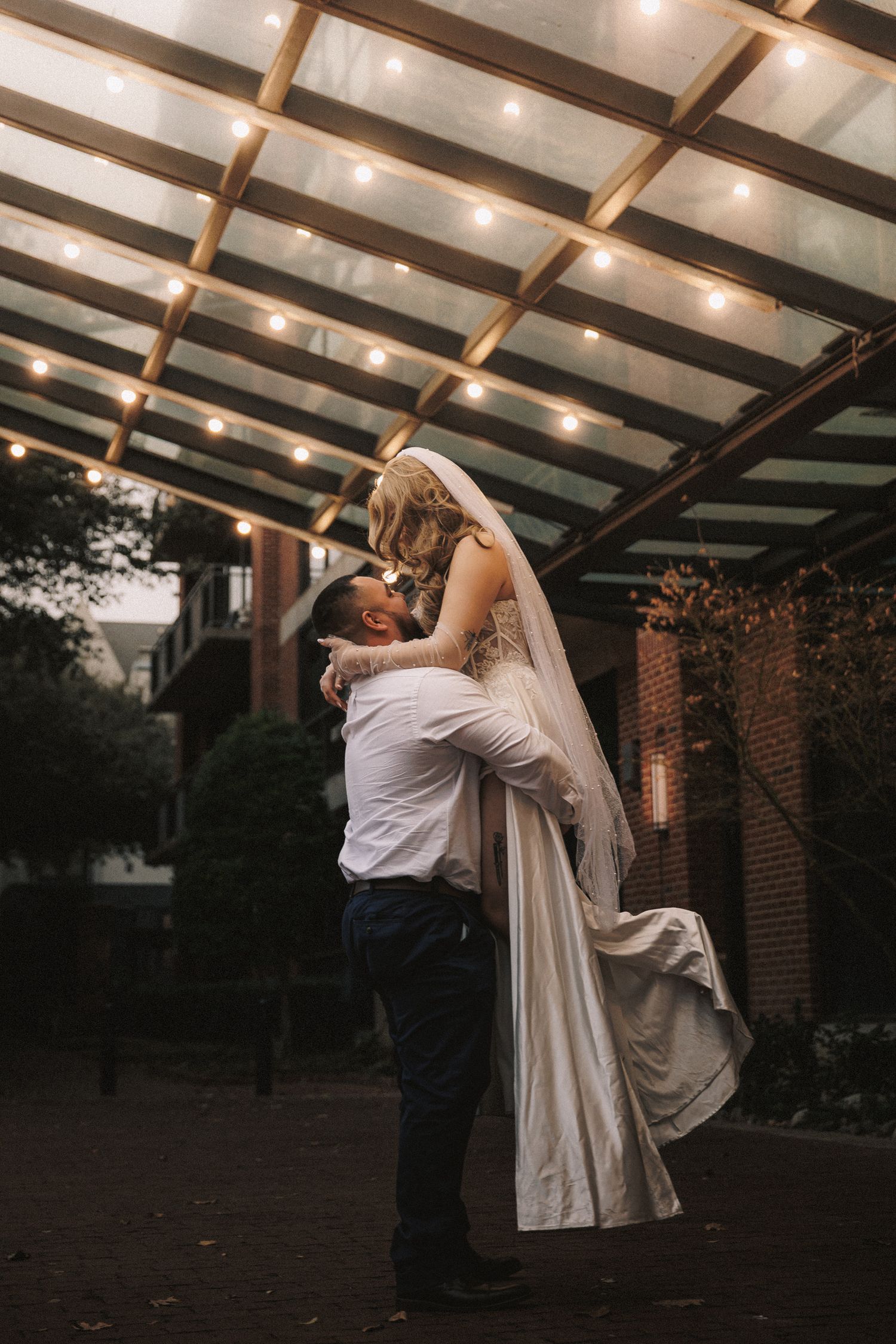 A couple dances romantically under a covered patio with warm lighting and exposed wooden beams.