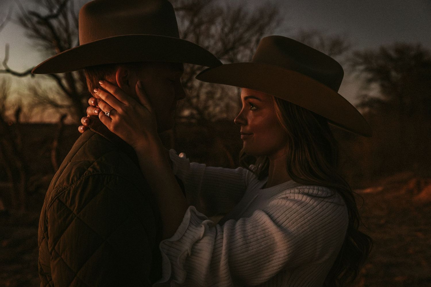 Romantic western-styled couple in hats share intimate moment at dusk.