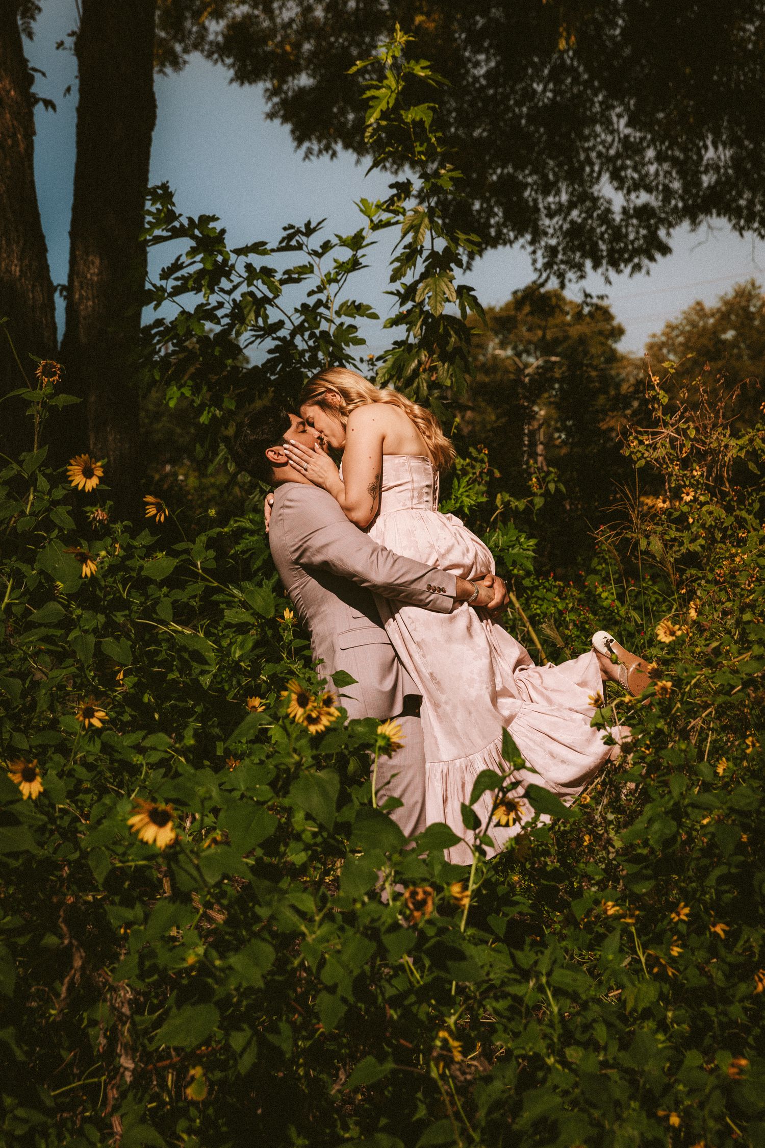 A romantic lift pose surrounded by green foliage and flowers in natural lighting.