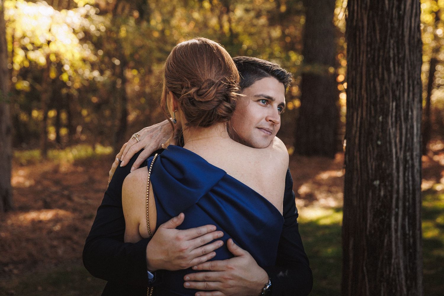 Two people share a warm embrace outdoors among autumn trees at a wedding.