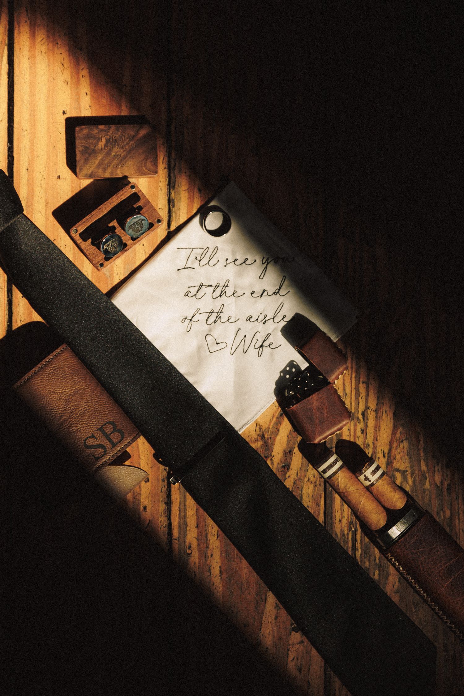 A handwritten note reading I'll see you at the end of the aisle, Wife, beside wedding accessories on wood.