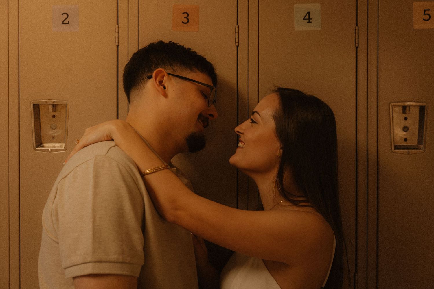 Couple sharing a romantic moment leaning against school lockers, smiling at each other tenderly.