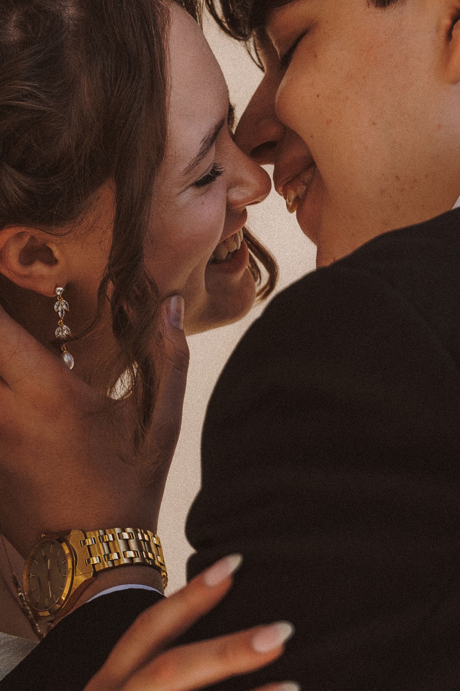 Close-up of laughing bride and groom touching foreheads, wearing gold bracelet and earrings.