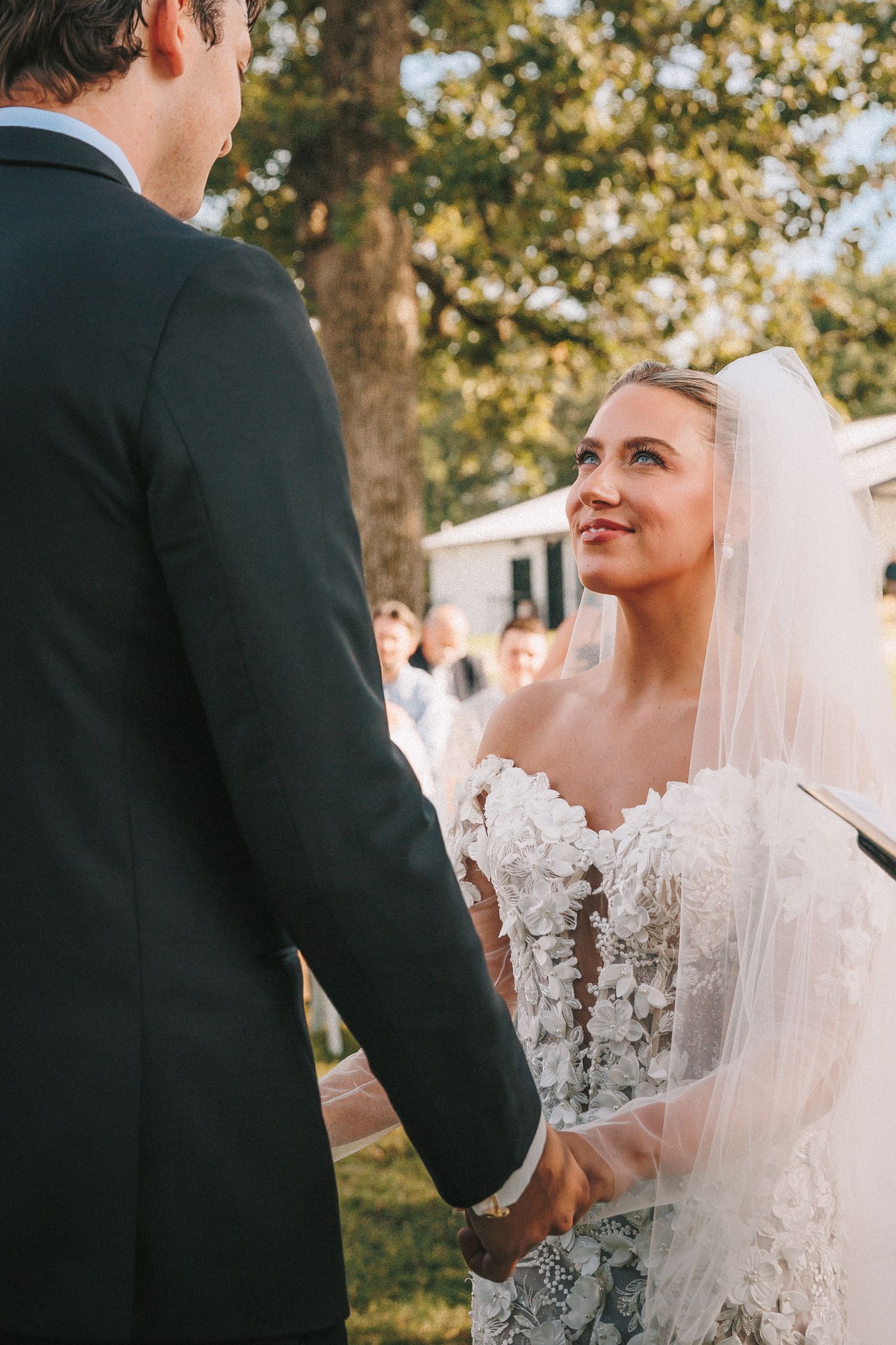 Bride and groom share a tender moment during their outdoor wedding ceremony among blossoming trees.