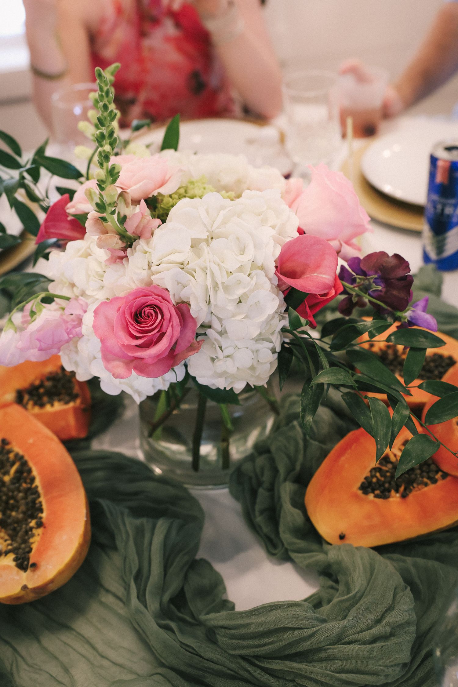 Wedding reception centerpiece with pink roses, white hydrangeas and green fabric on dining table.