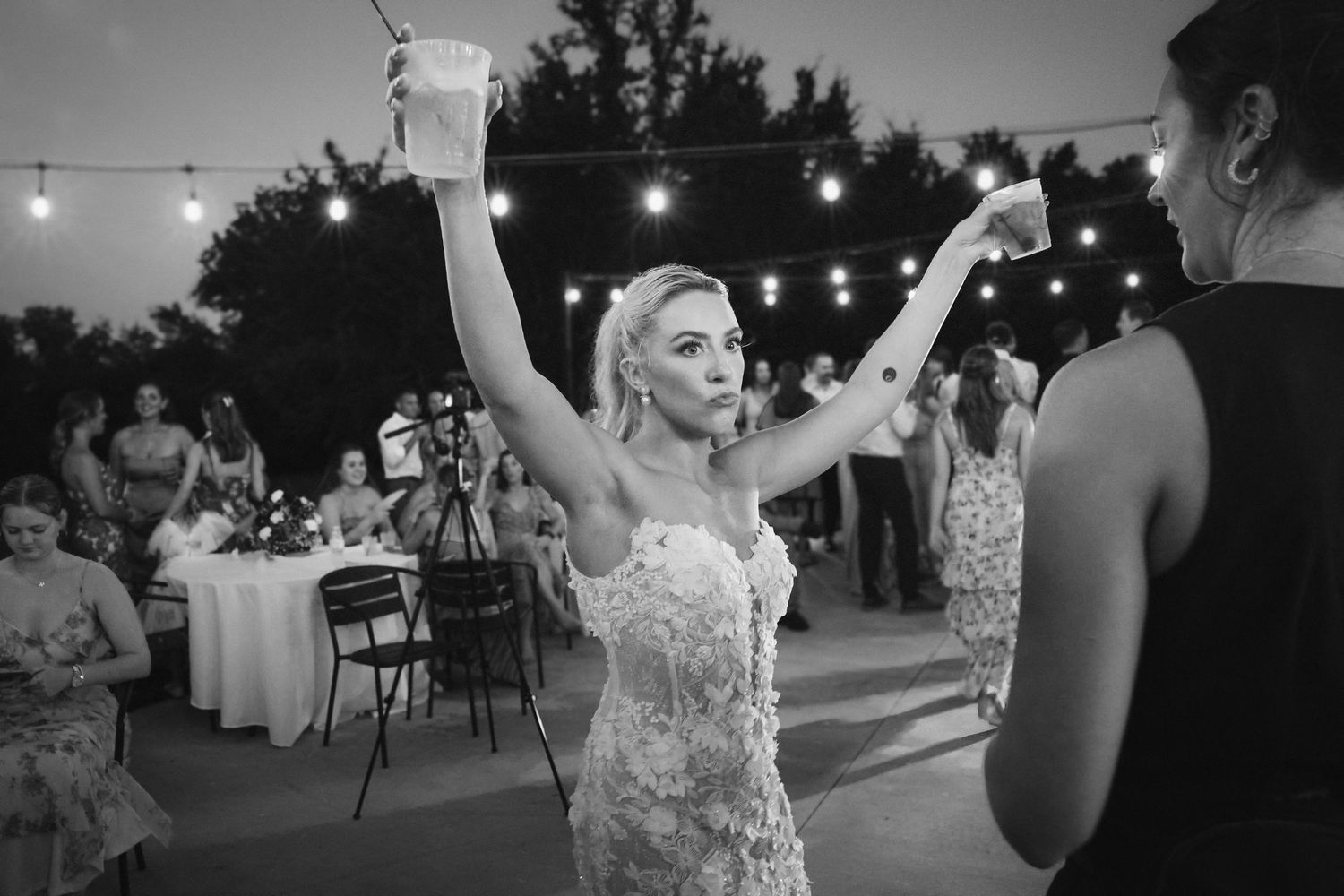 Black and white photo of wedding reception with string lights creating ambient atmosphere.