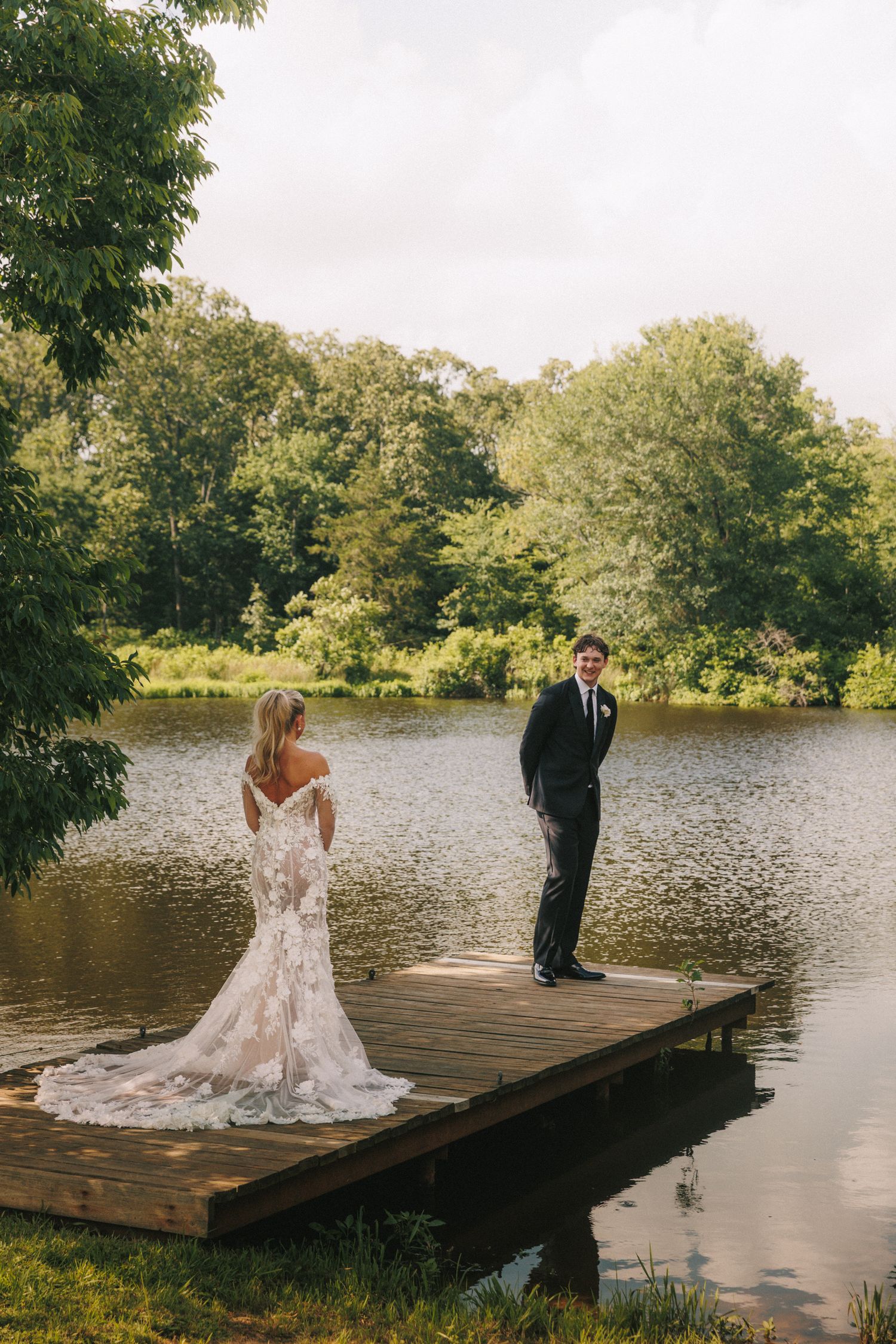 Couple standing apart on wooden dock for romantic wedding photo.