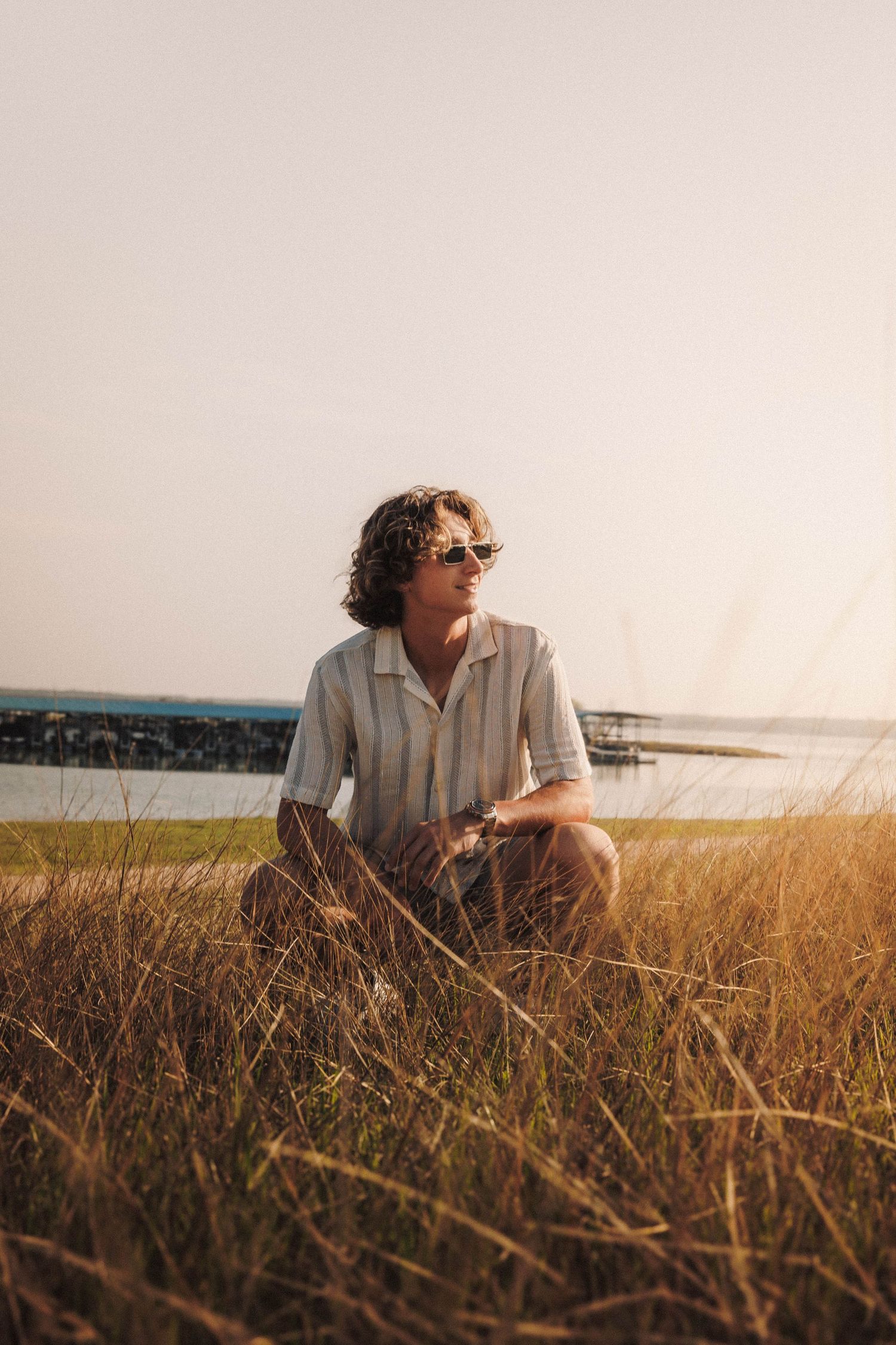 Person wearing sunglasses sits in golden field during sunset hours creating peaceful outdoor portrait.