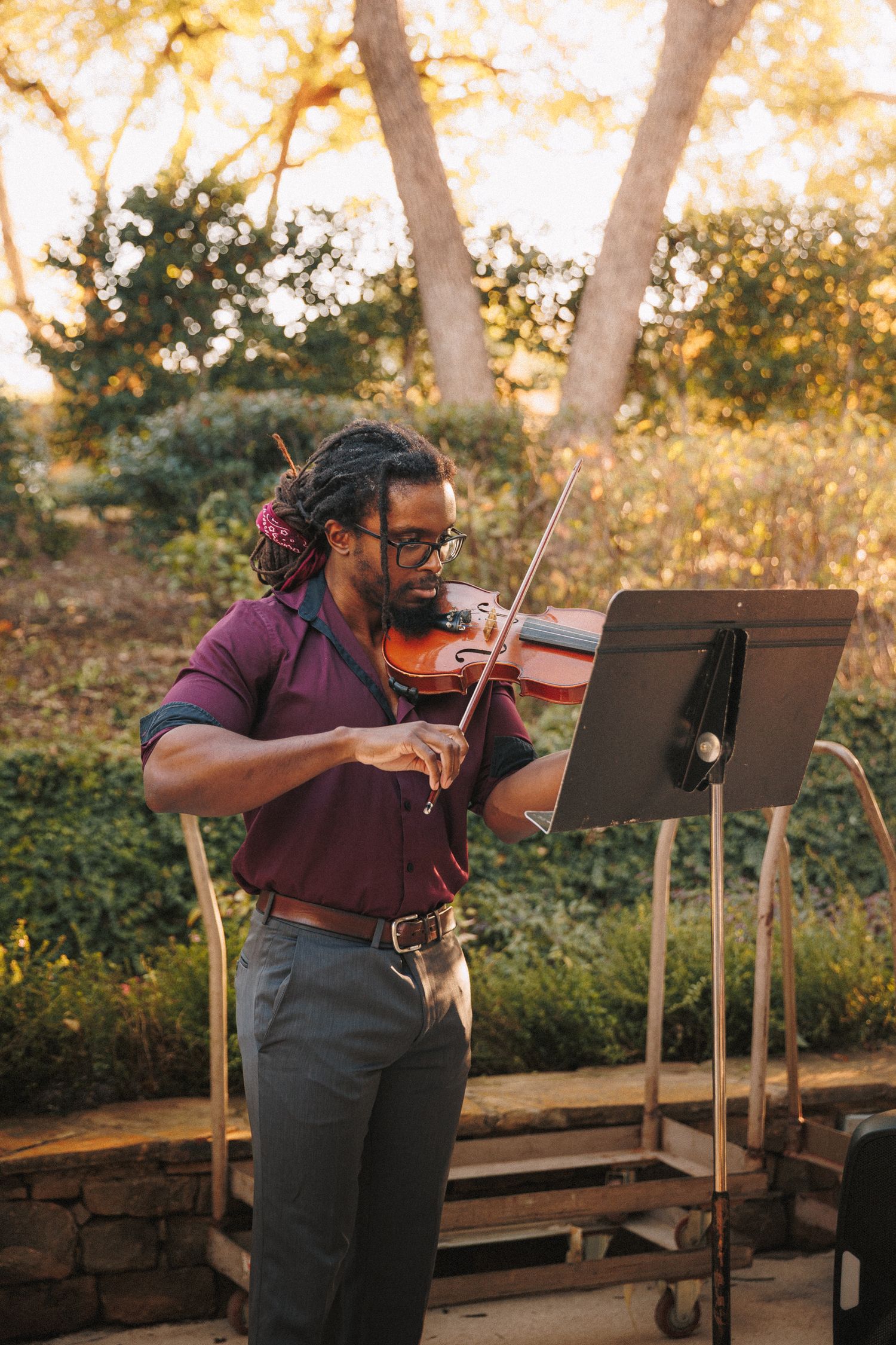 Violinist in burgundy shirt performs outdoor wedding ceremony music at golden hour in garden.