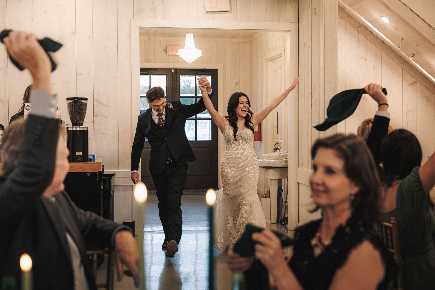 Bride and groom make a grand entrance into their wedding reception as guests cheer and celebrate.