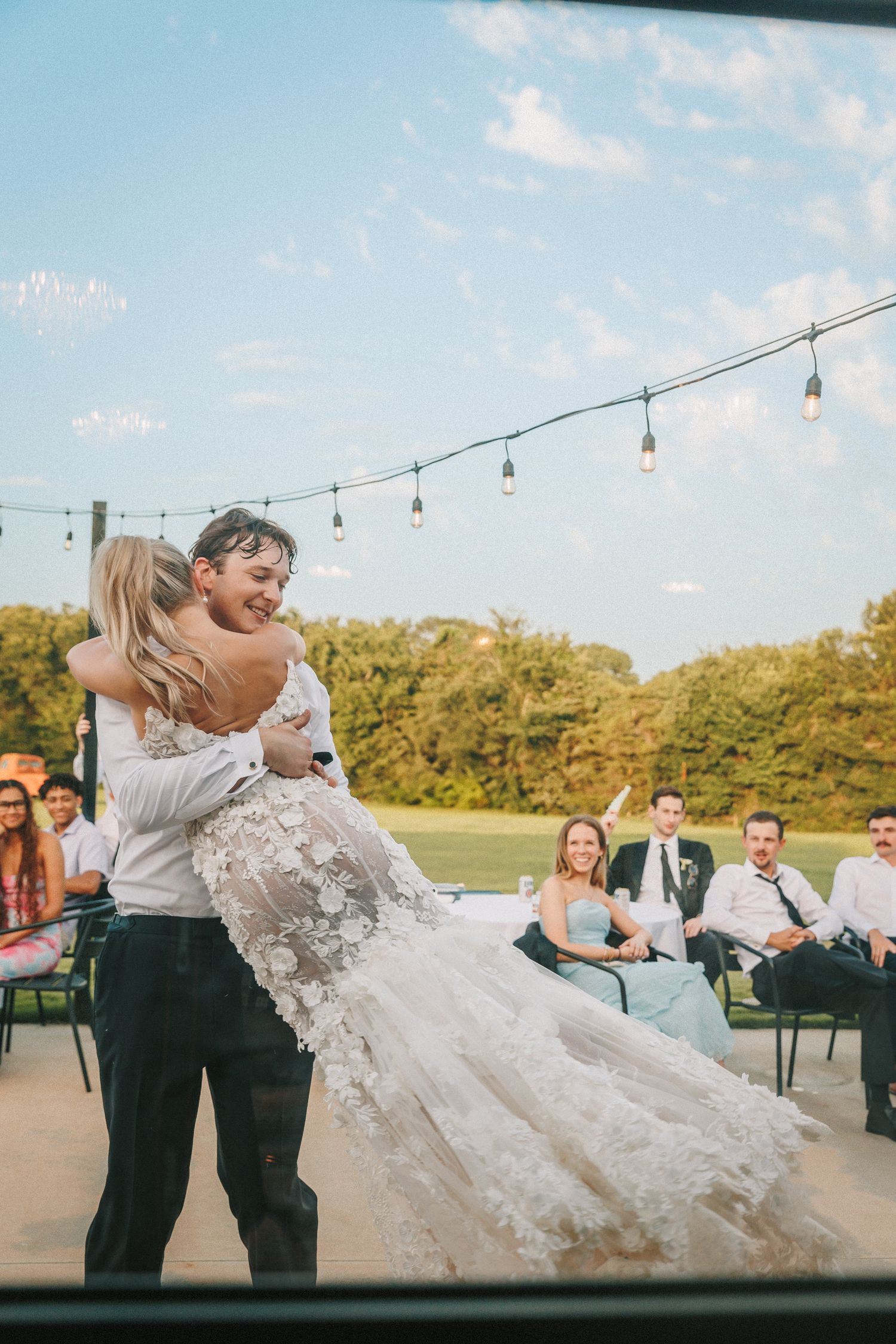 Wedding couple performs a romantic dip dance move on an outdoor patio under string lights at sunset.