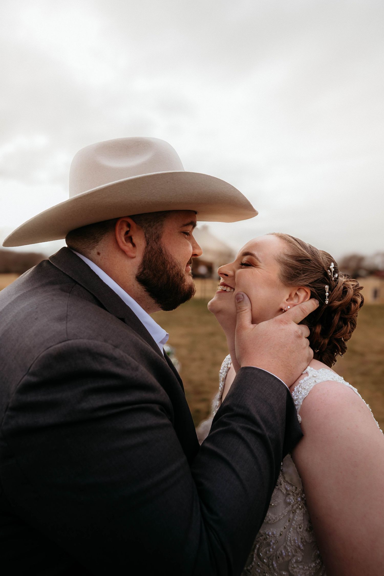 An intimate moment between newlyweds outdoors, with the groom wearing a cowboy hat and dark suit during their rustic wedding.