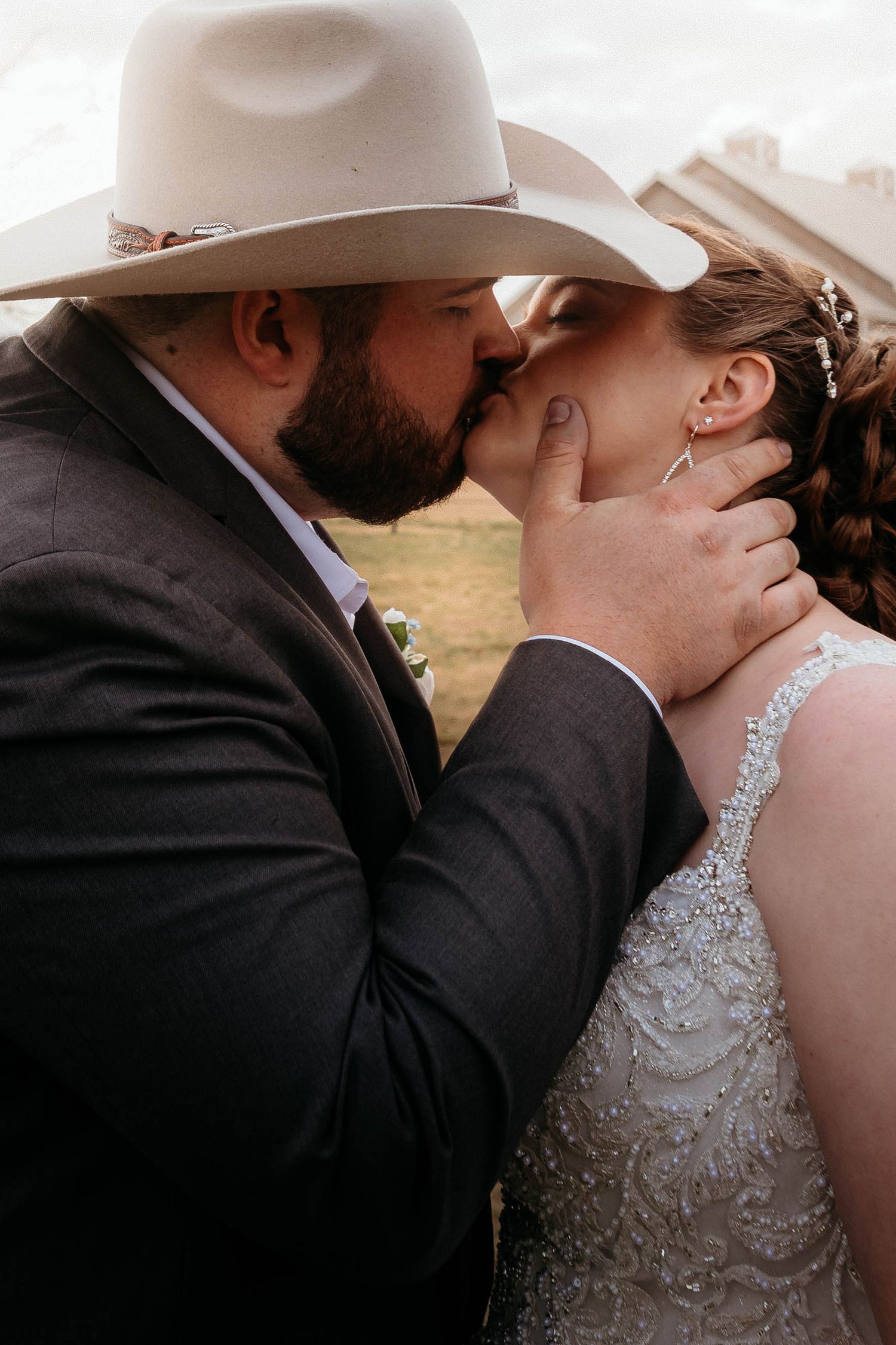Couple in western wedding attire sharing an intimate moment in front of a rustic background.