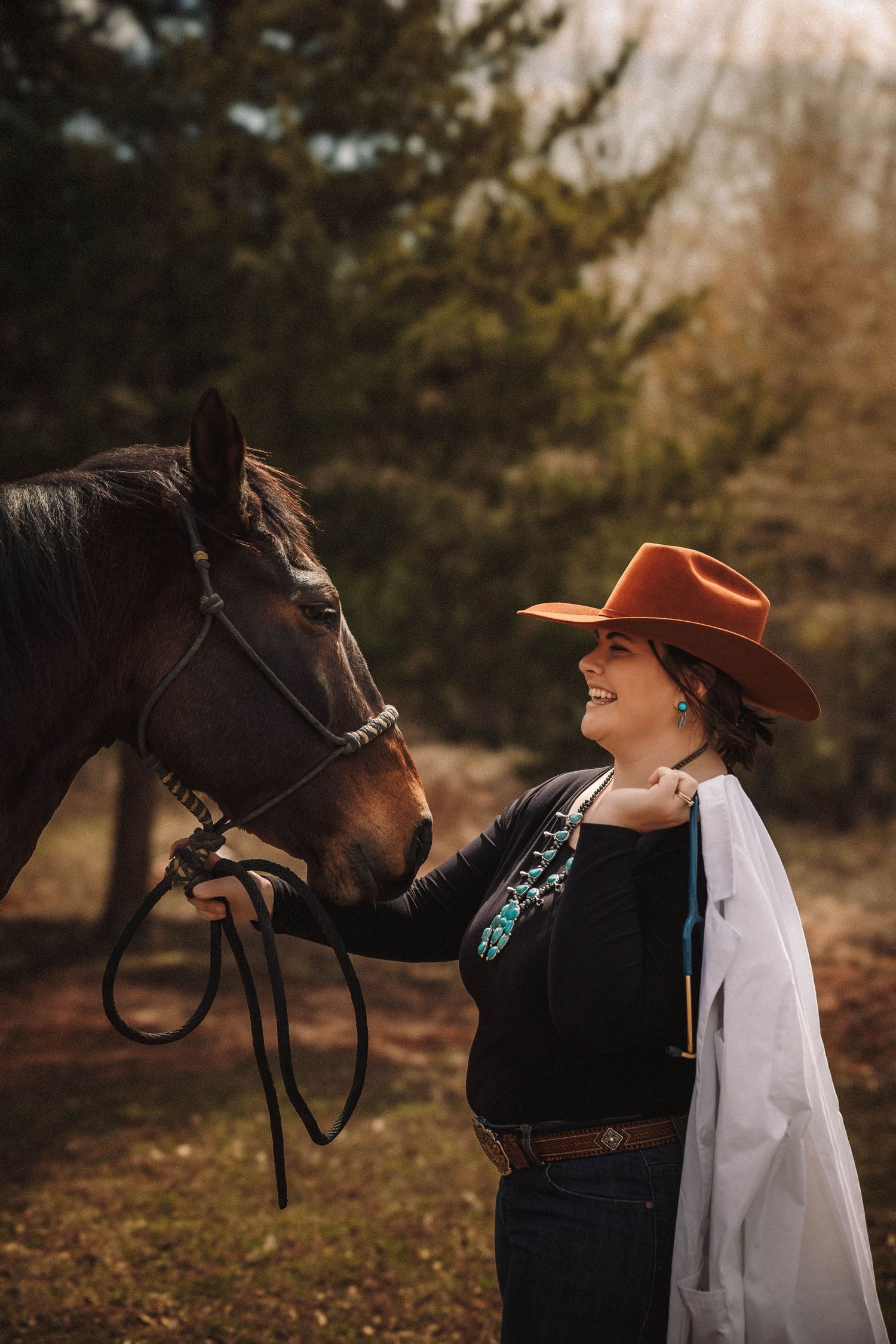 A heartwarming interaction between a person in brown hat and white top with a dark horse against an autumn backdrop.