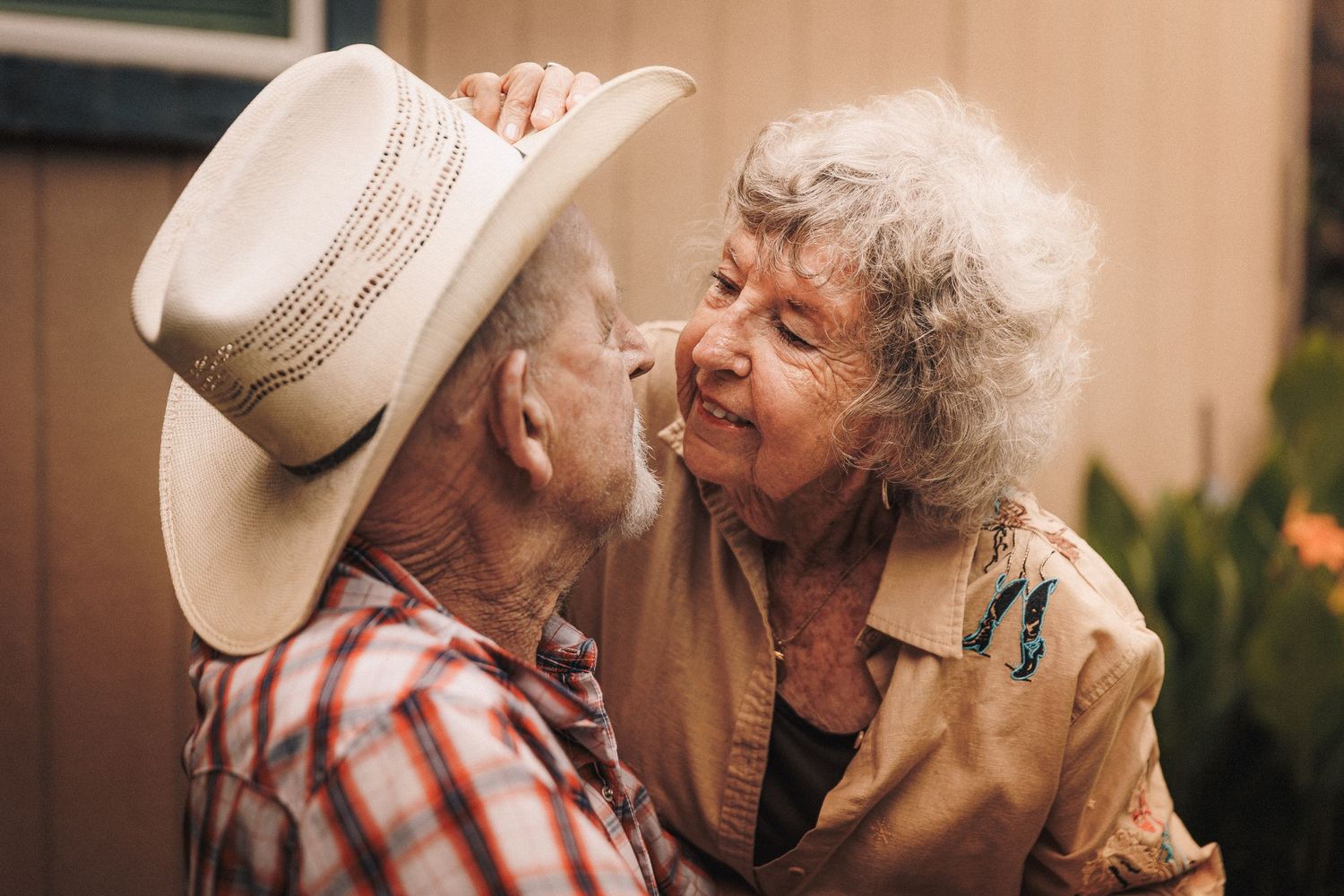 A couple in western attire shares an intimate poolside moment at sunset with a white cowboy hat.