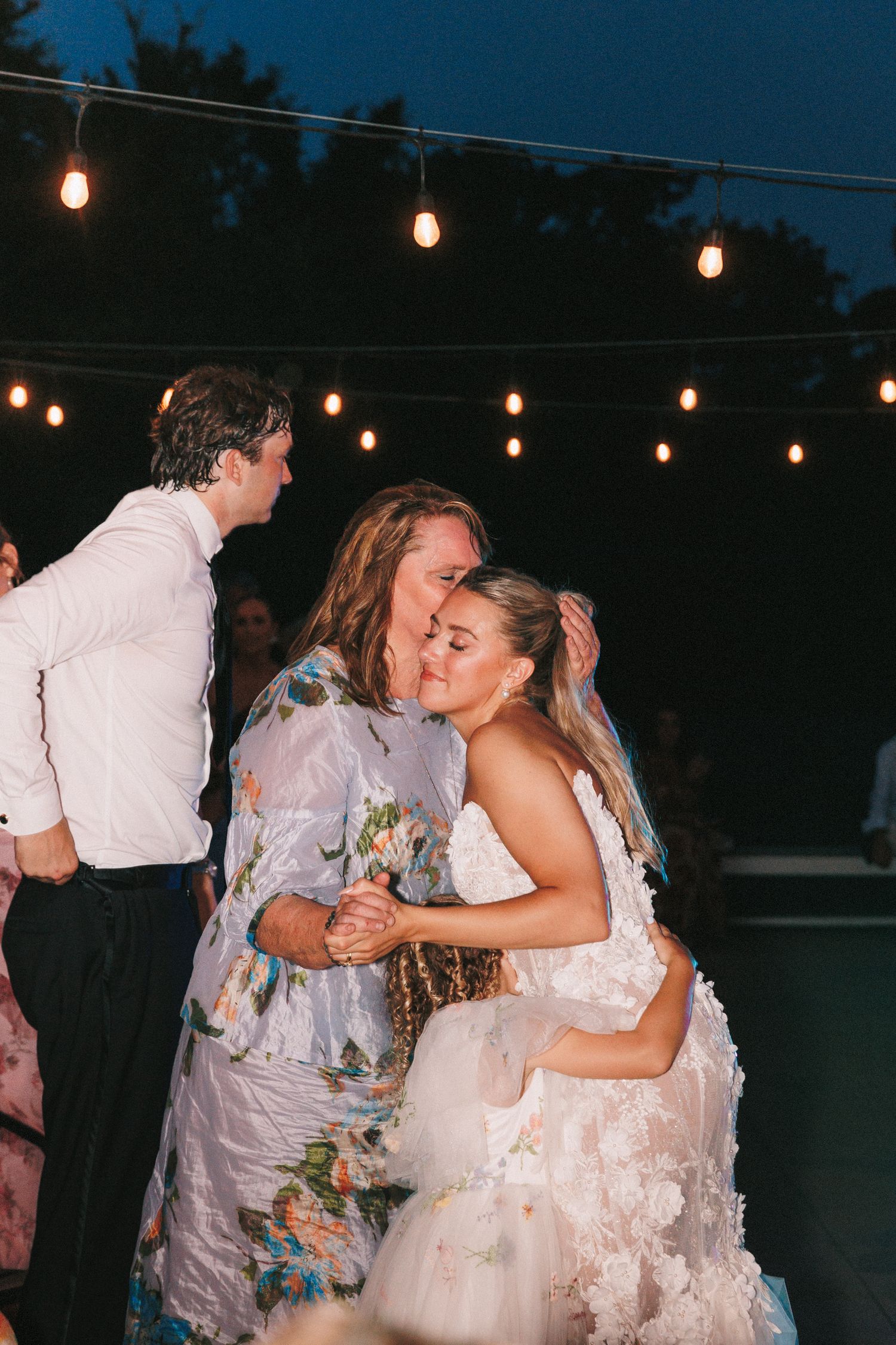 Wedding guests dancing under string lights at an outdoor evening reception.