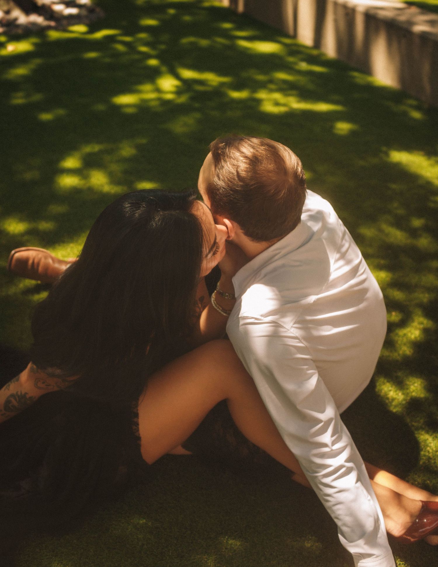 Person in white shirt lies on grass under dappled sunlight in a tranquil garden setting.