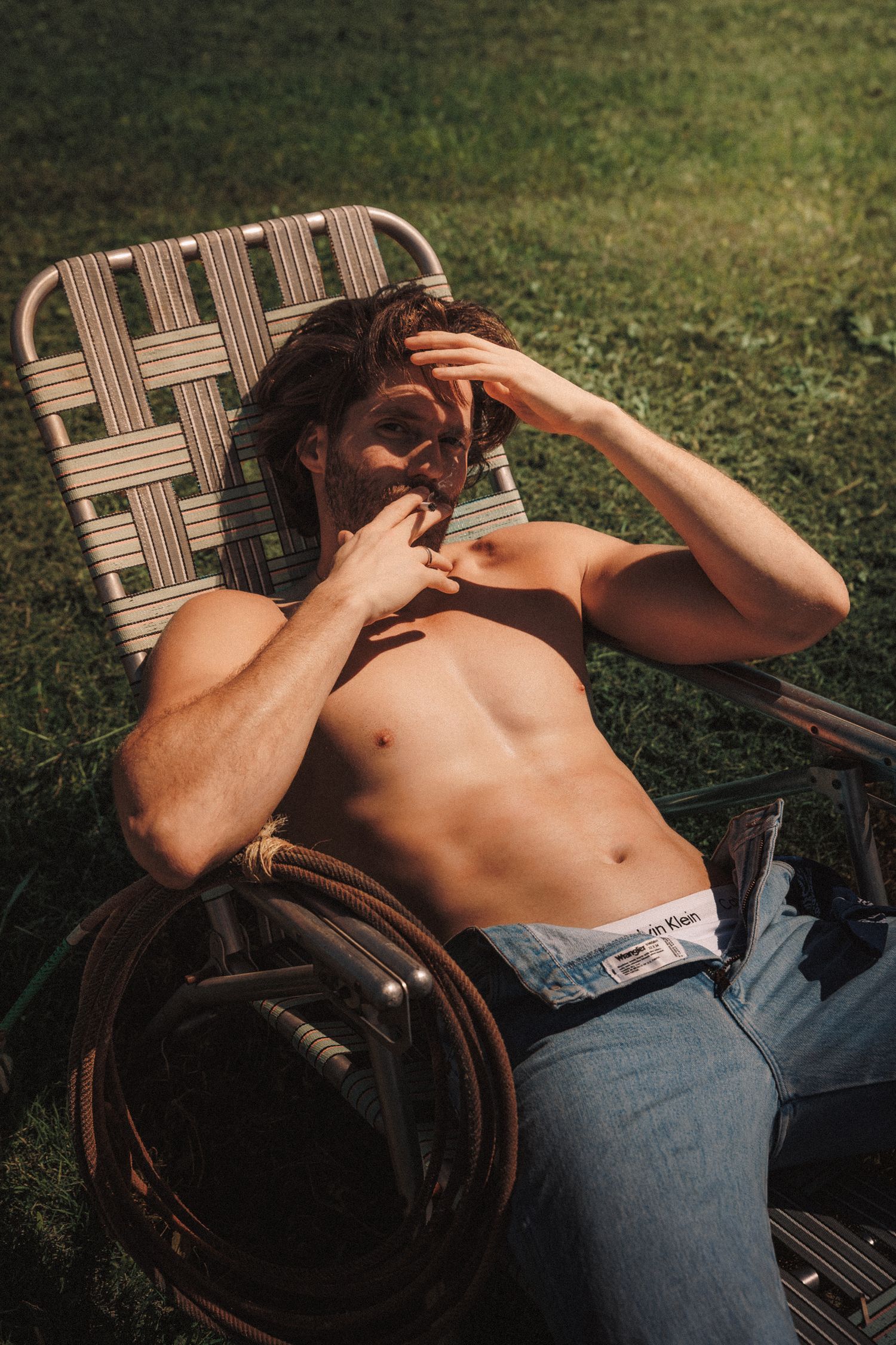 Person relaxing in brown outdoor lounge chair on grass during a sunny day.