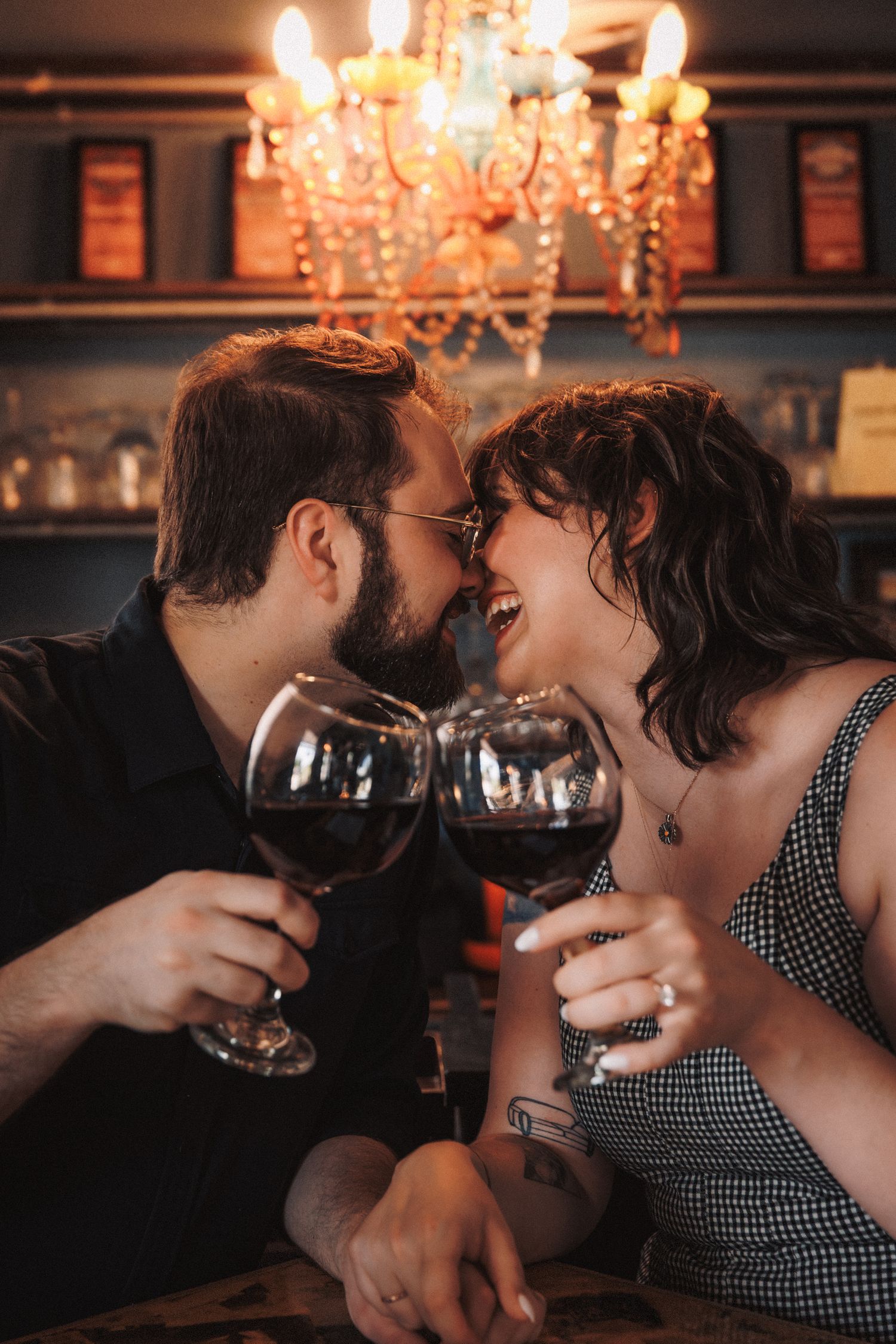 A romantic couple sharing wine glasses and intimate moments in a chandelier-lit restaurant atmosphere.