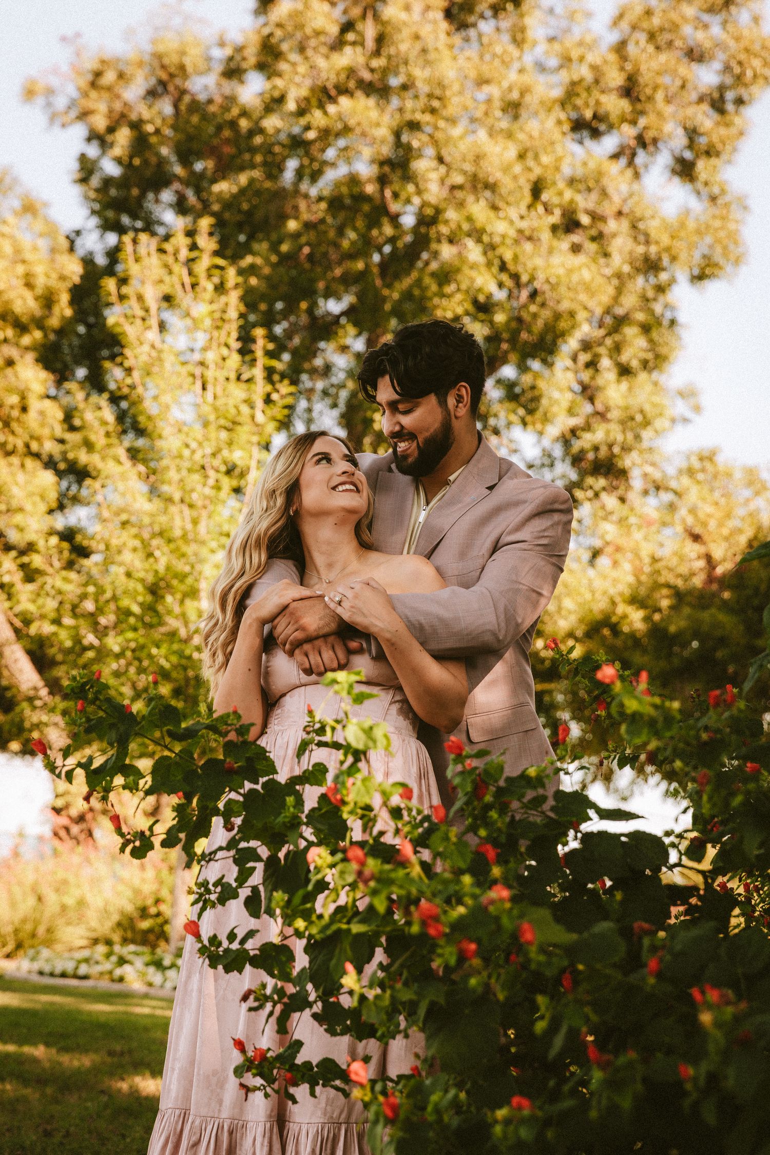 Intimate couple shares tender moments among blooming flowers in a sun-drenched garden setting.