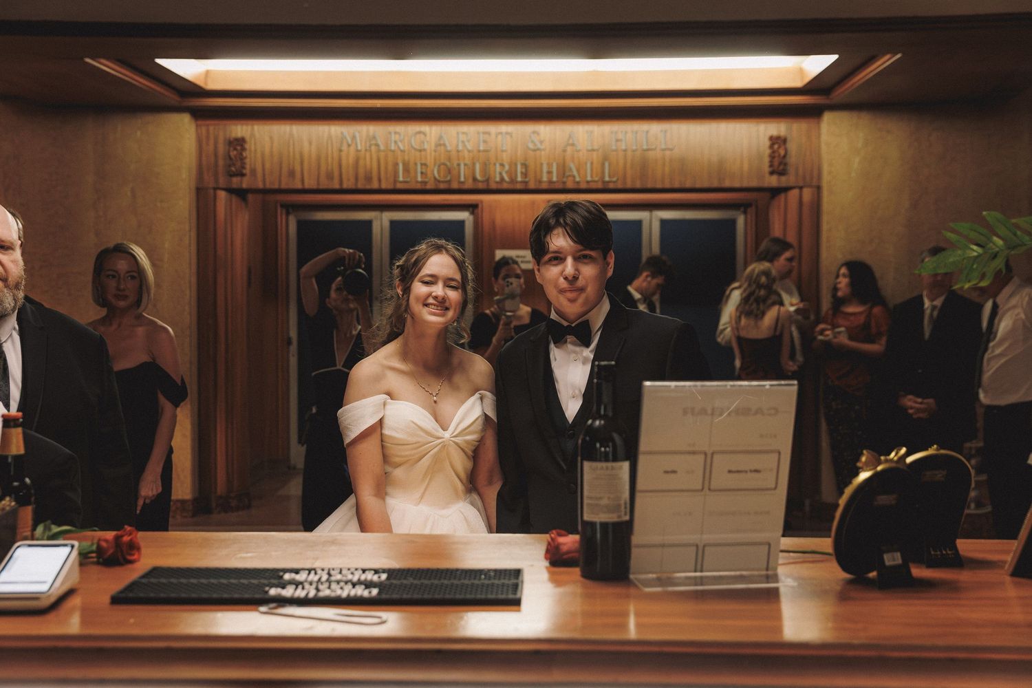 Smiling bride and groom standing together at a reception venue check-in table.