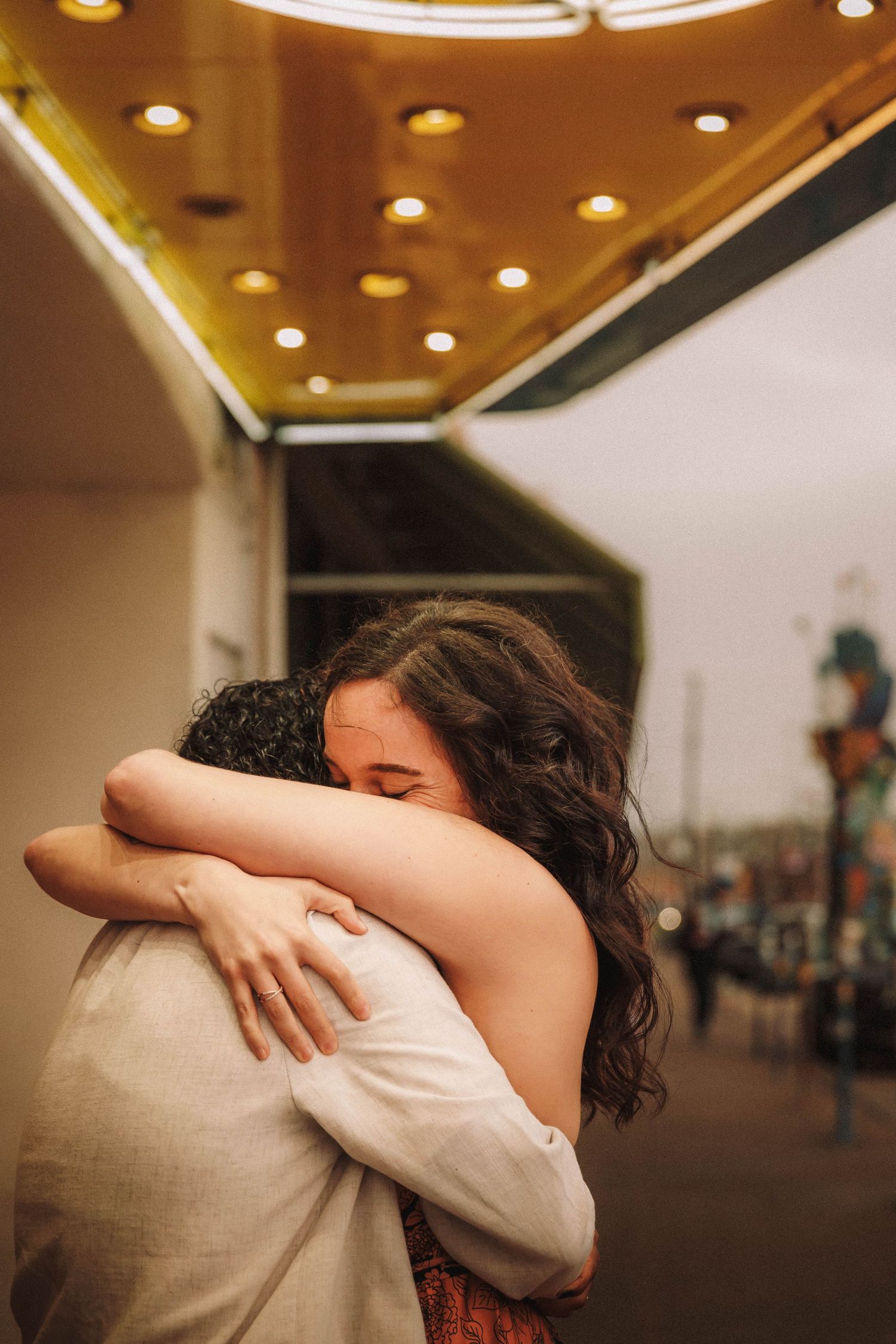 Couple sharing a heartfelt hug outside a theater under warm glowing marquee lights.