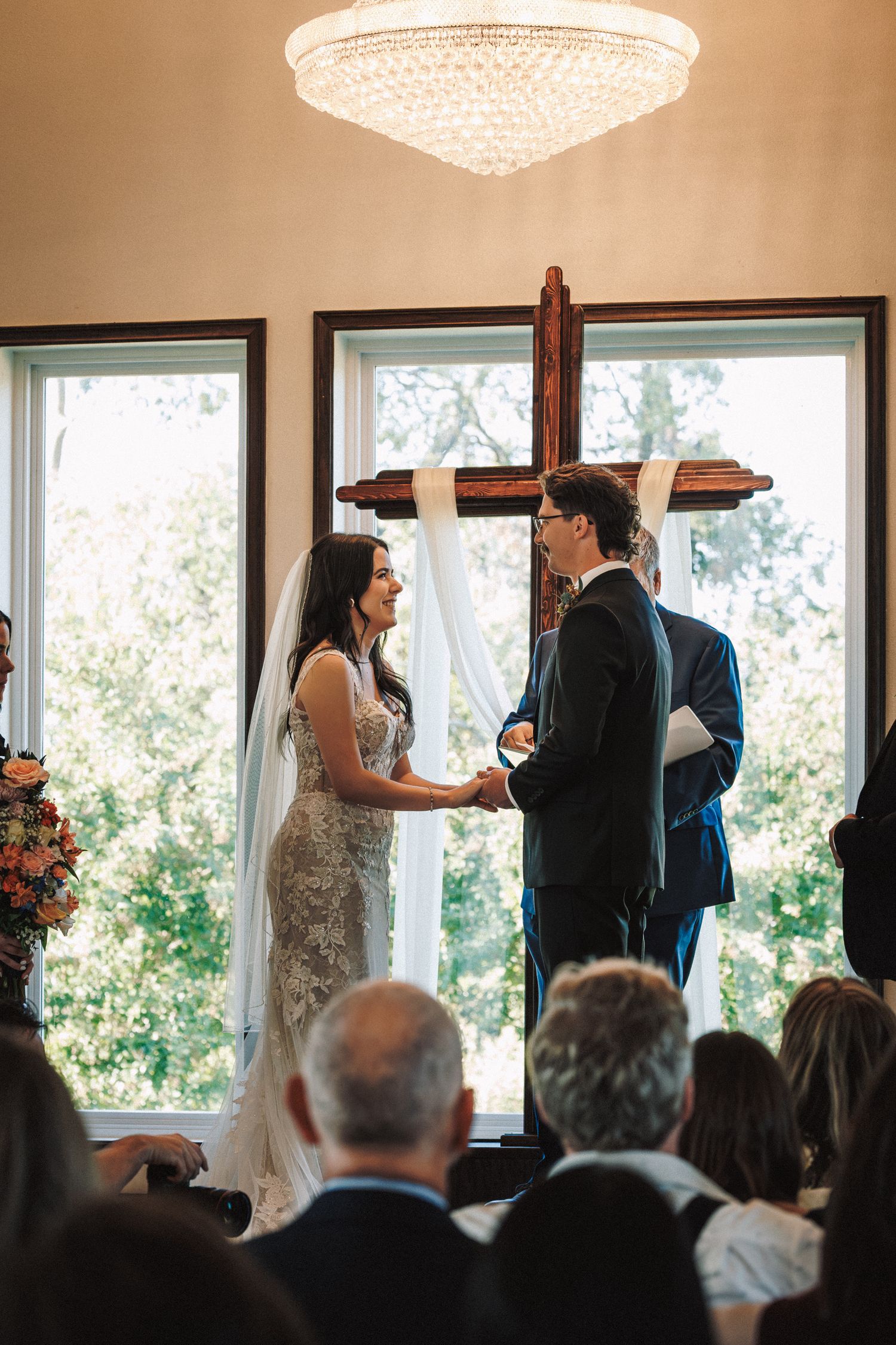 Bride and groom exchanging vows at a chapel altar beneath a wooden cross with floral arrangements.