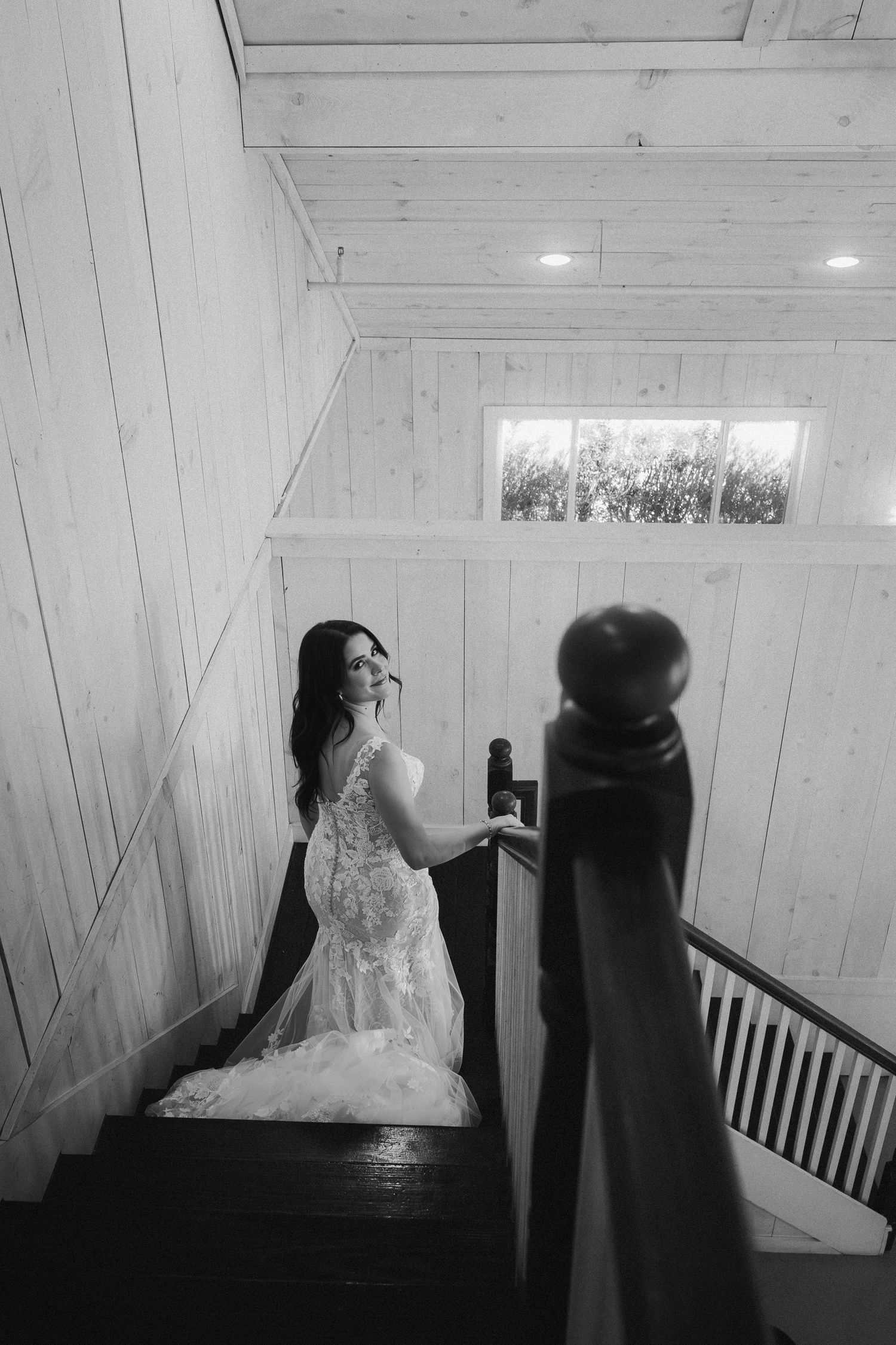 Black and white photo of a bride in a lace mermaid gown on a wooden staircase.