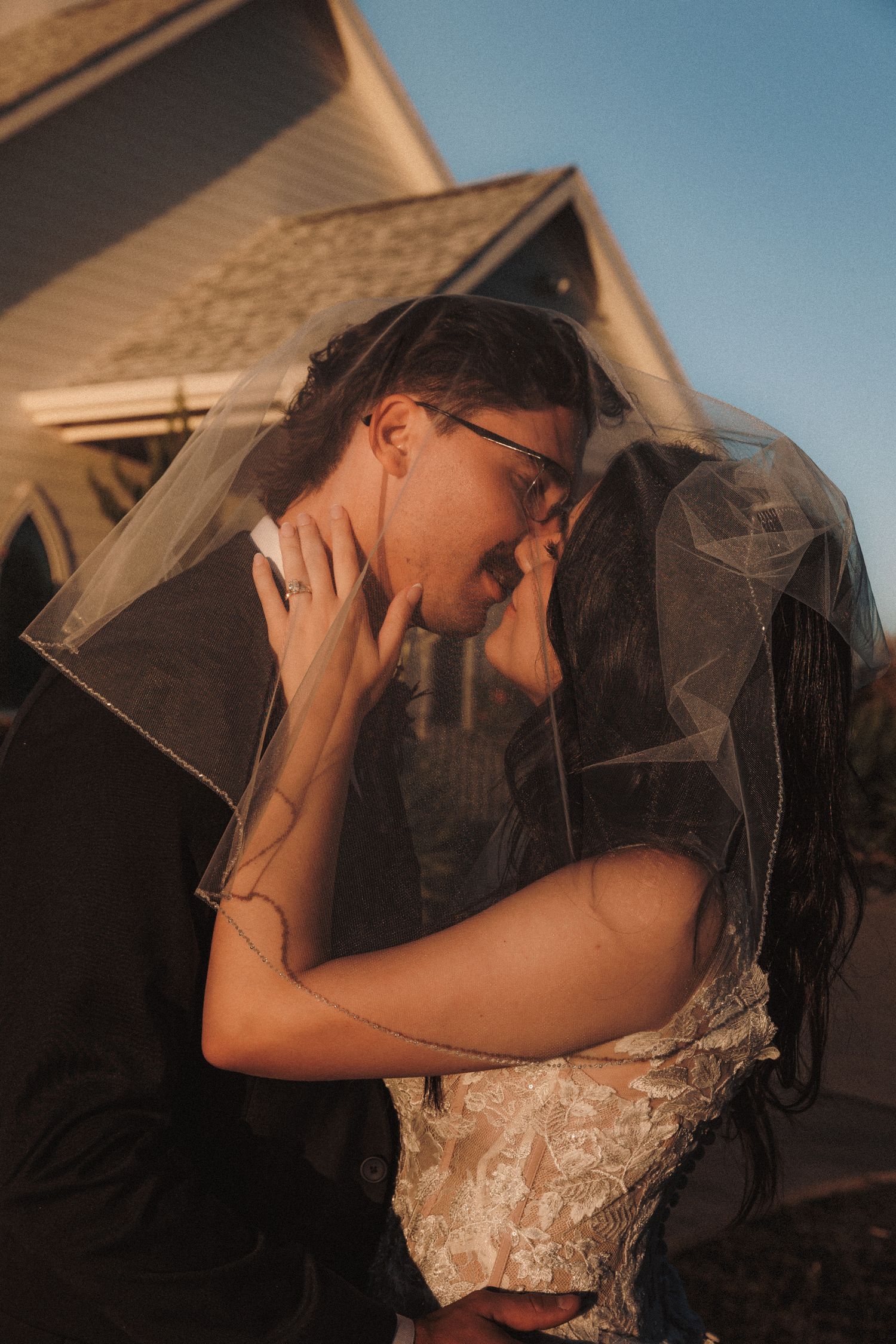 Bride and groom share romantic kiss under veil at golden hour.