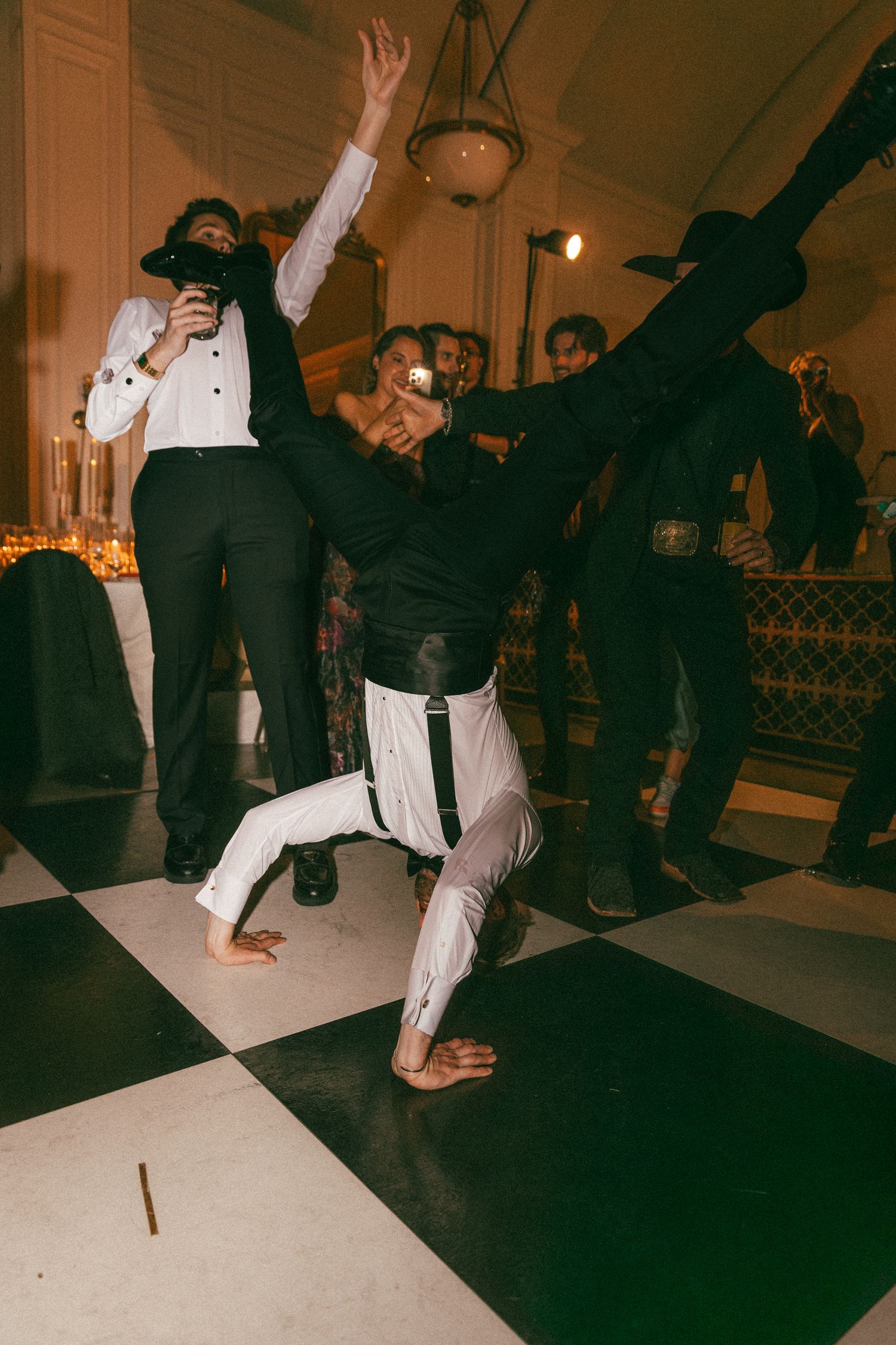 A performer does a breakdance move on a checkered dance floor at a wedding reception.
