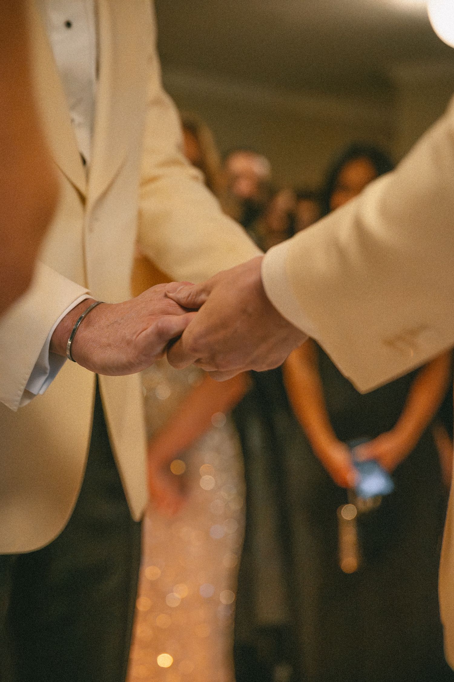 Two grooms in matching ivory tuxedo jackets hold hands during their wedding reception dance.