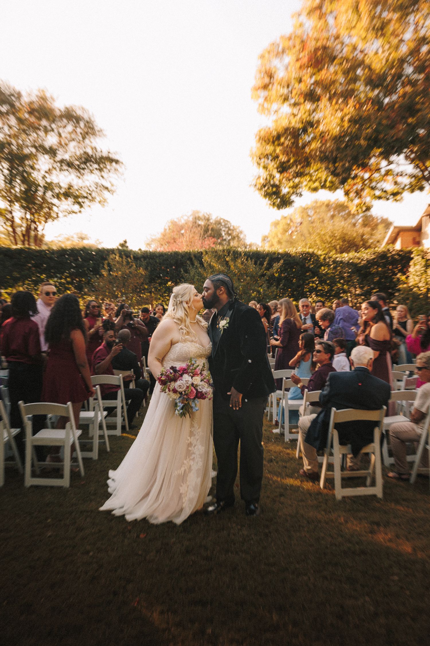 Newlyweds share a kiss while walking back down the aisle at outdoor fall wedding ceremony.