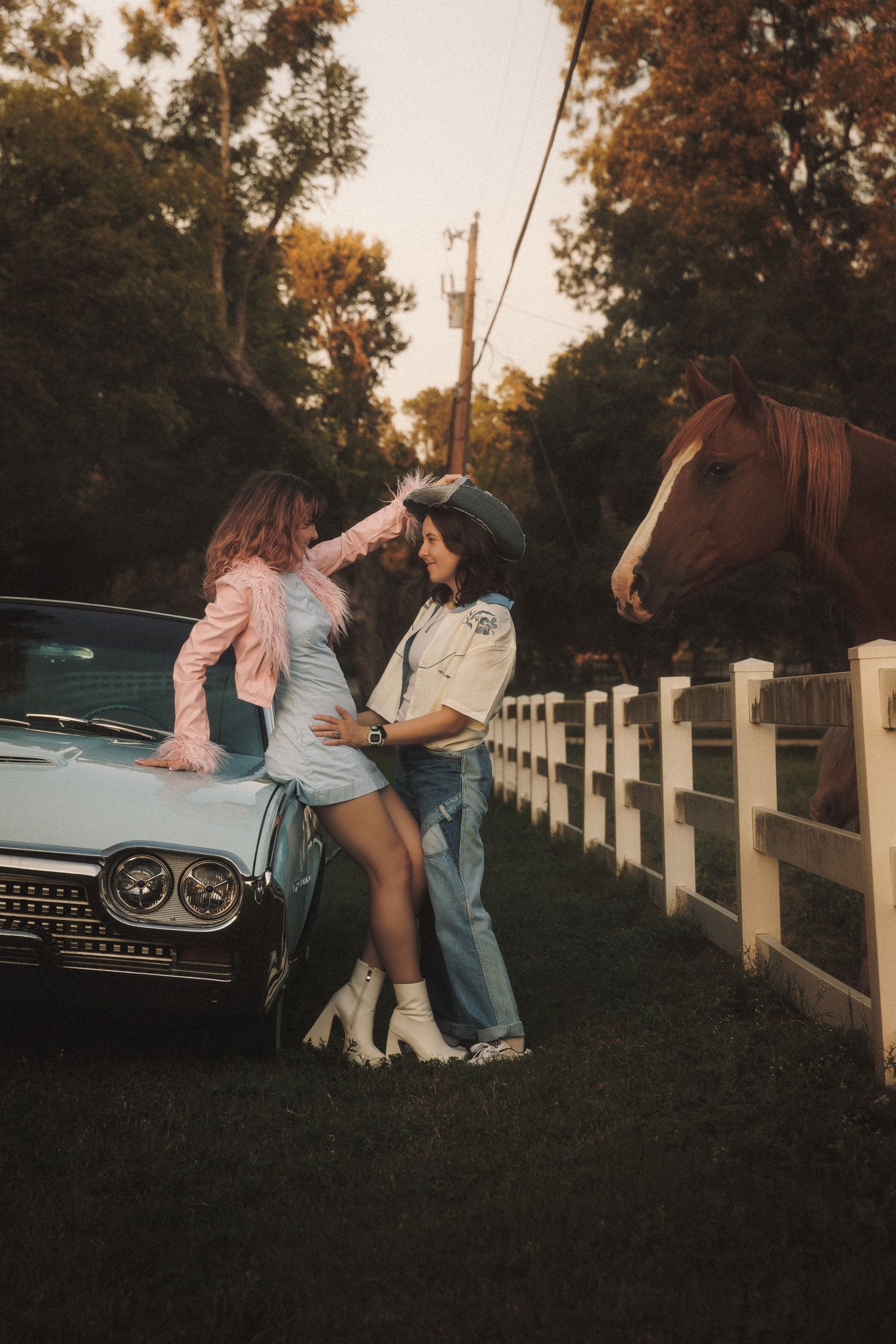 A romantic couple shares tender moments by a vintage car and white fence at sunset in a cinematic photoshoot.