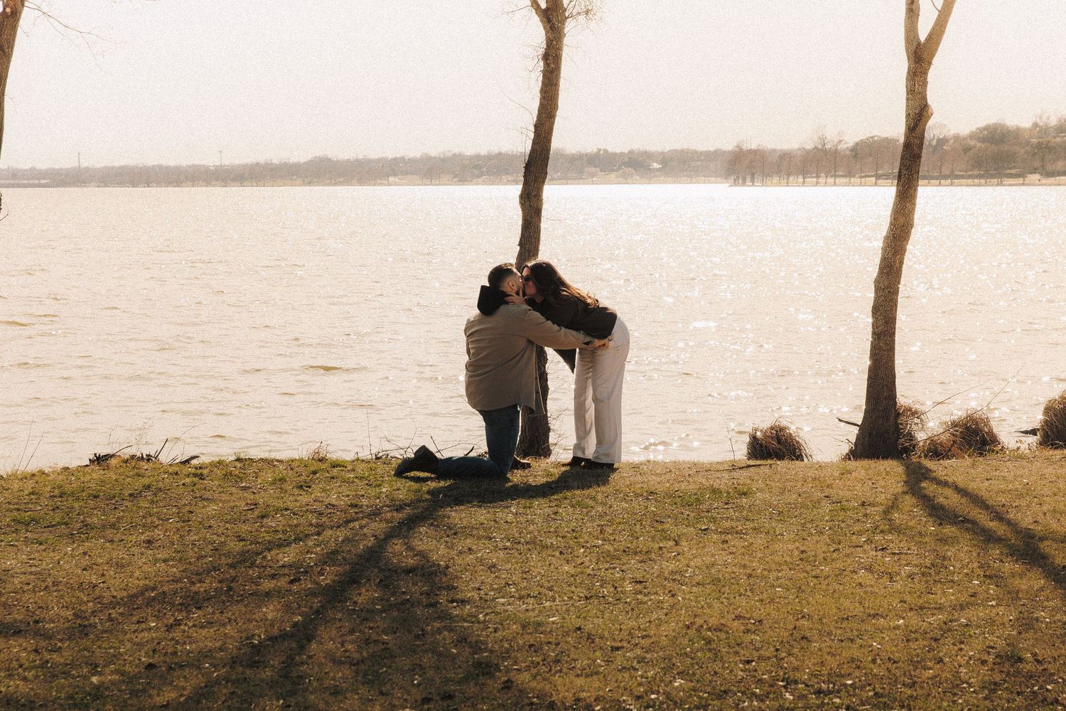 A couple sharing a special moment by a lake during golden hour with trees in the background.