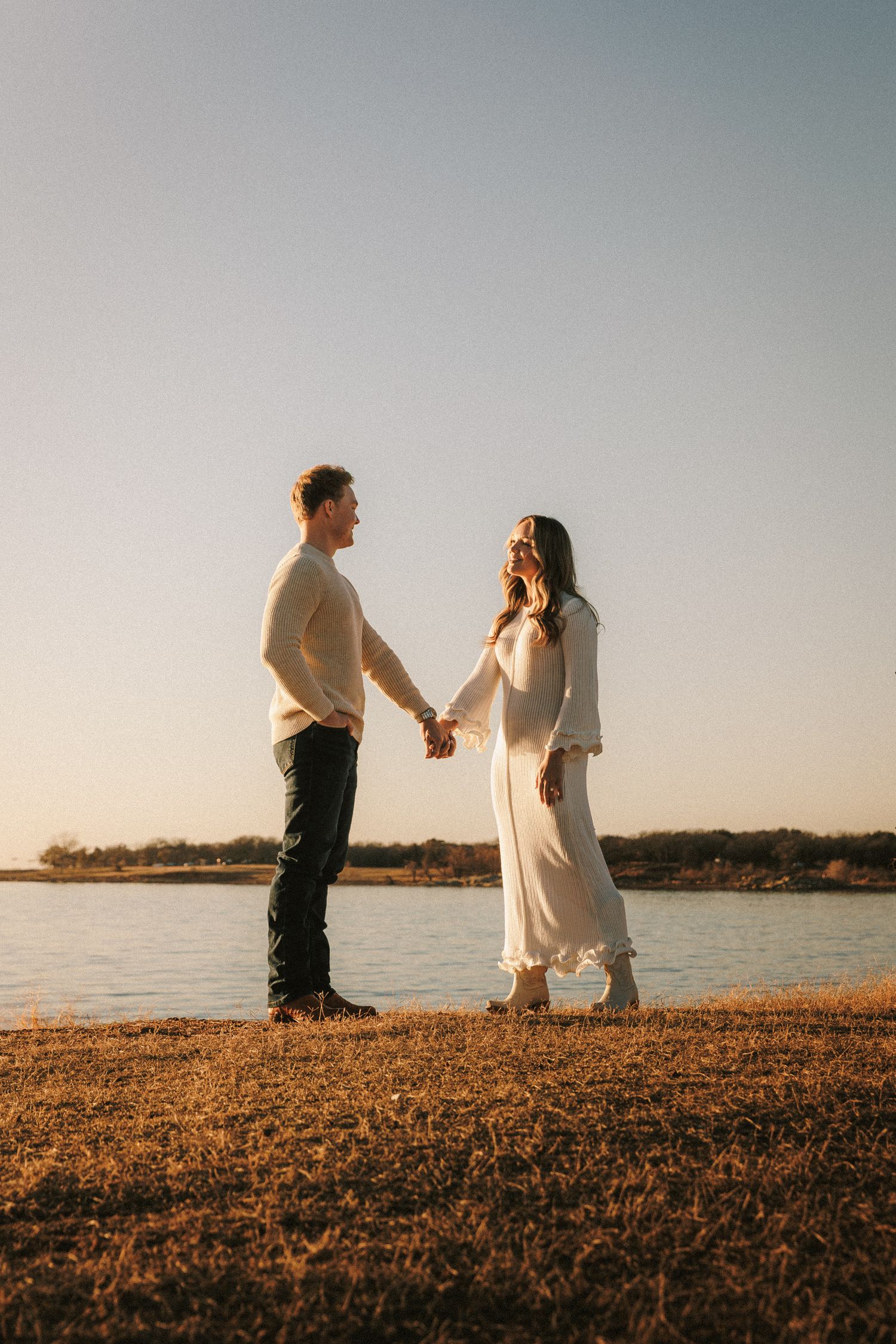 A couple shares tender moments while walking along a waterfront path during sunset.