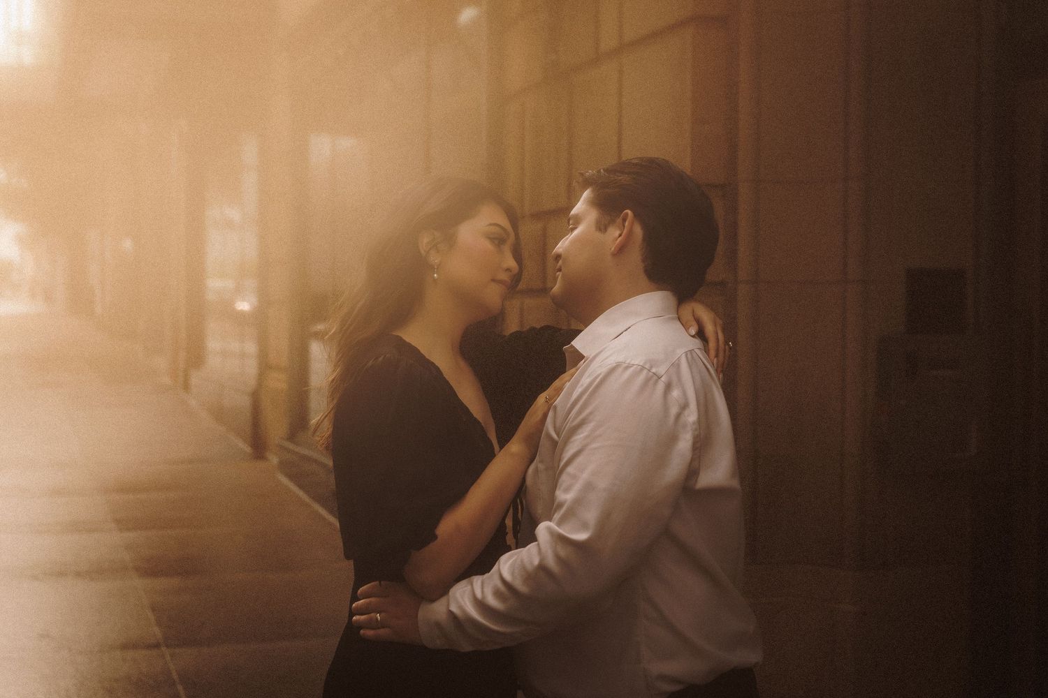 Couple sharing a romantic embrace on a misty city sidewalk bathed in warm golden light at dusk.