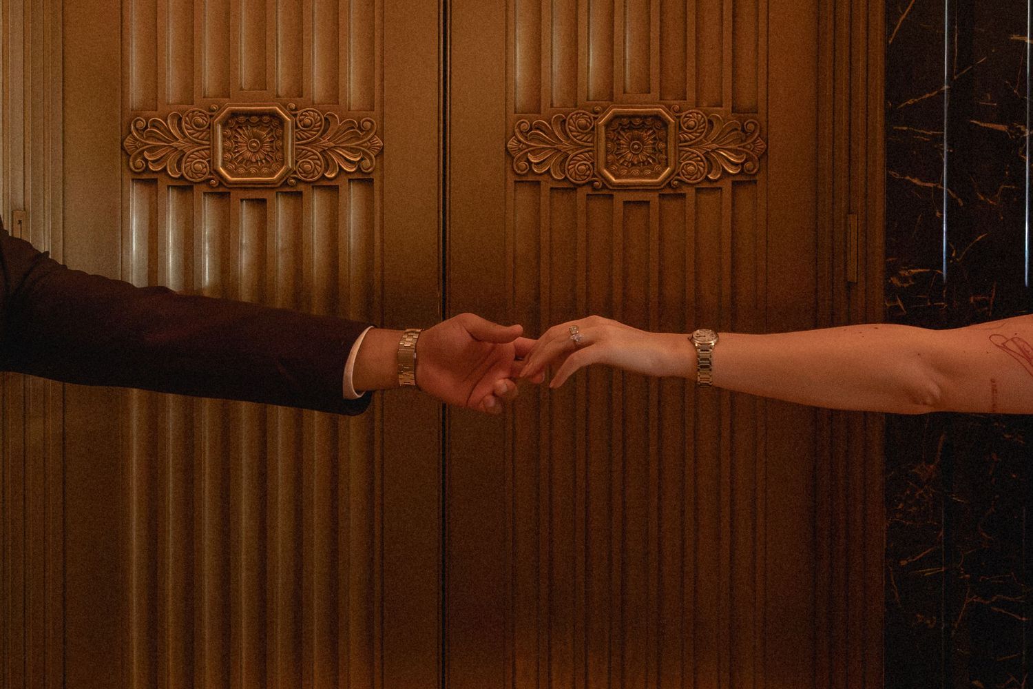 Close-up of a couple holding hands in front of ornate wooden doors.