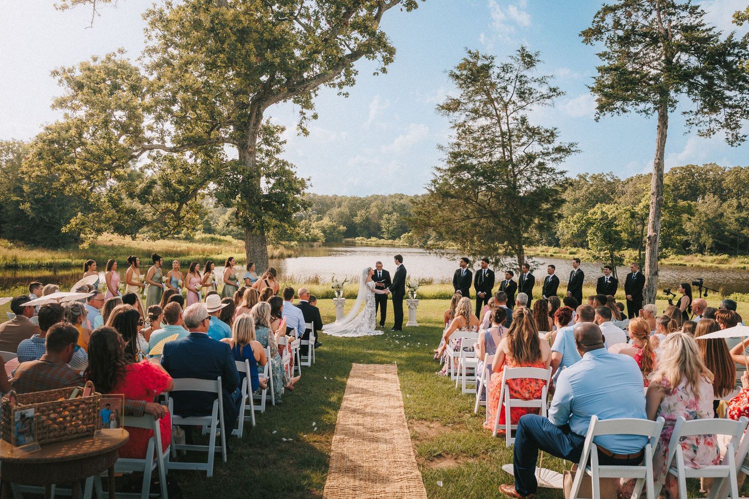 Rows of white chairs set up for an outdoor lakeside wedding ceremony with guests arriving.