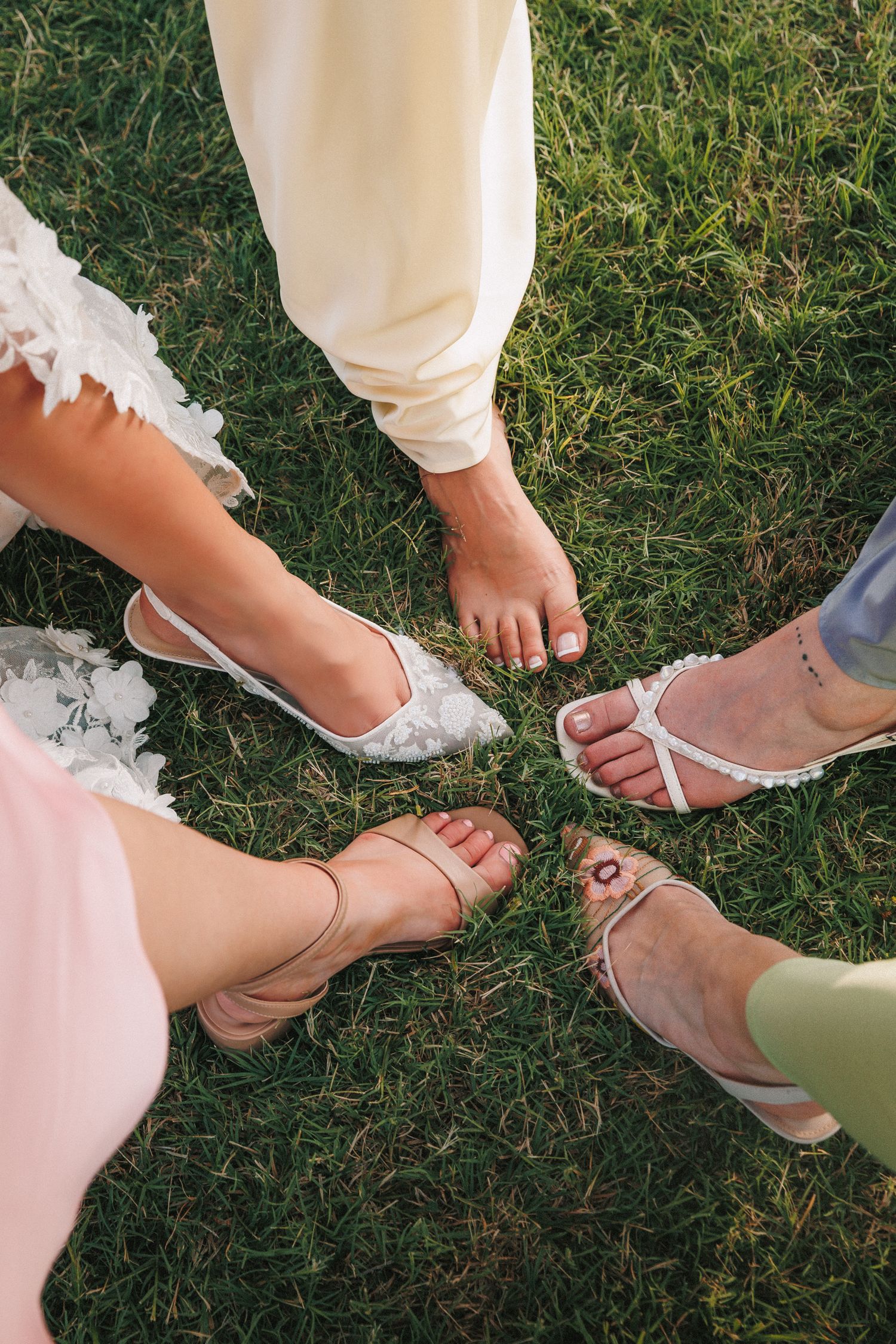 Close-up of wedding guests' feet wearing elegant sandals on grass.